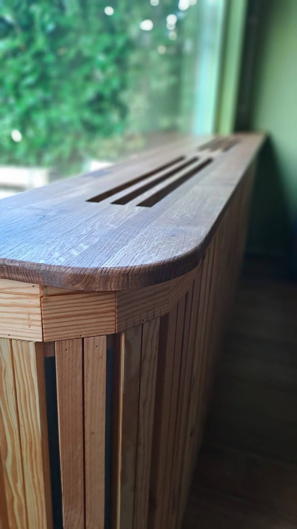 Houten radiatorombouw naast een raam met groen bladerend uitzicht