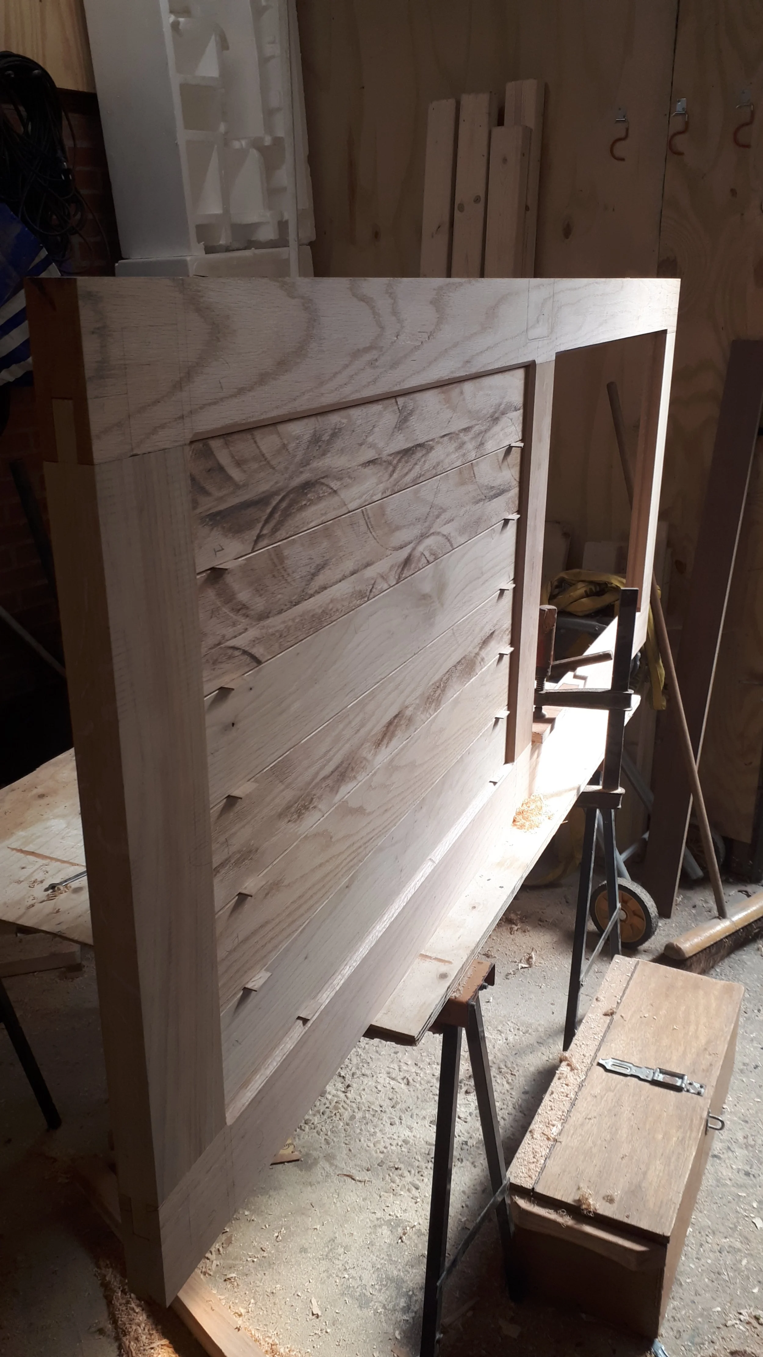 Een houten meubelstuk dat wordt gemaakt, mogelijk een bed of een kast, in een werkplaats. Het hout is onbewerkt en de constructie is nog niet voltooid.