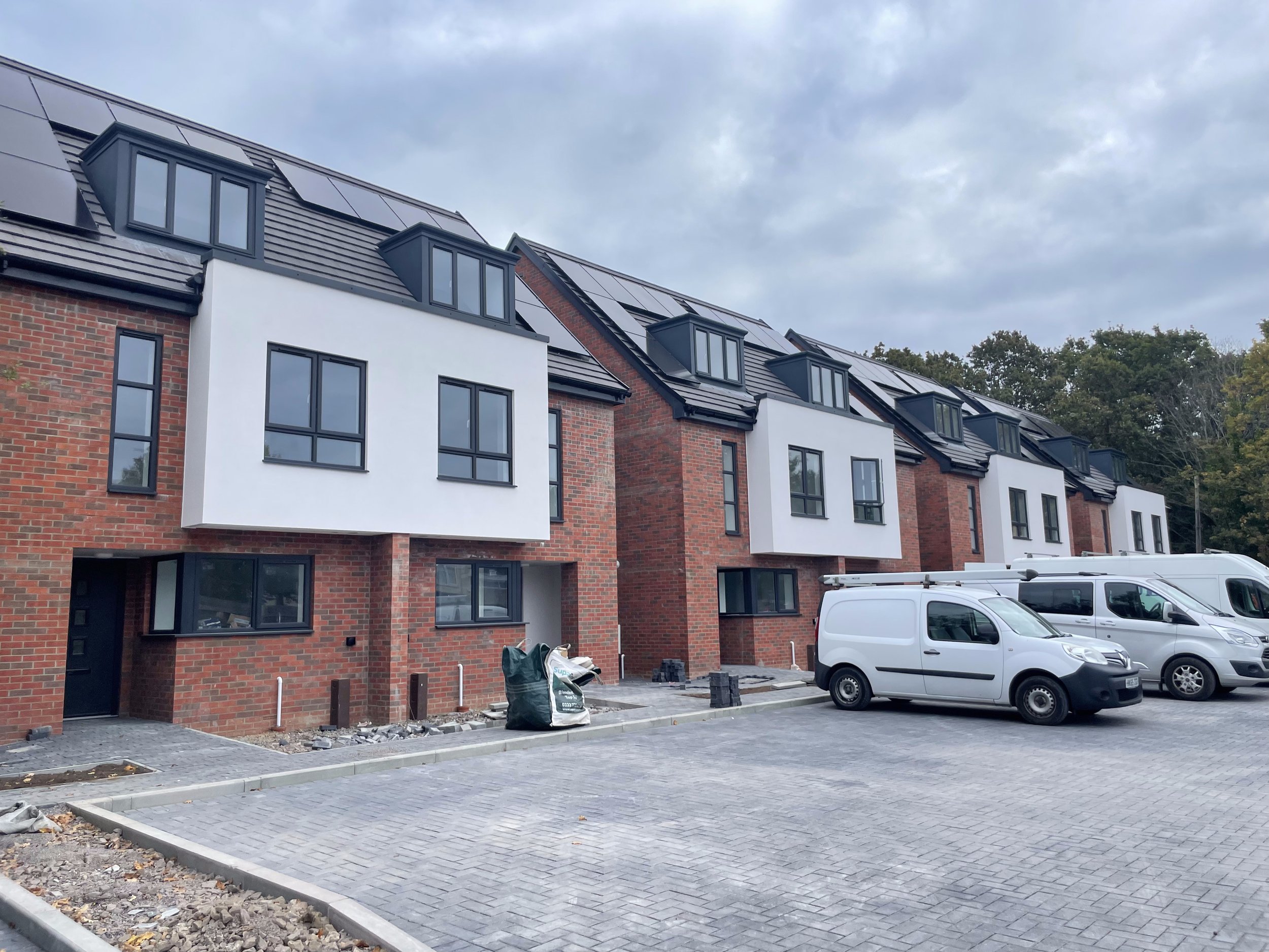 Modern multi-story residential buildings under construction with partially finished exteriors and a parking lot with white vans.