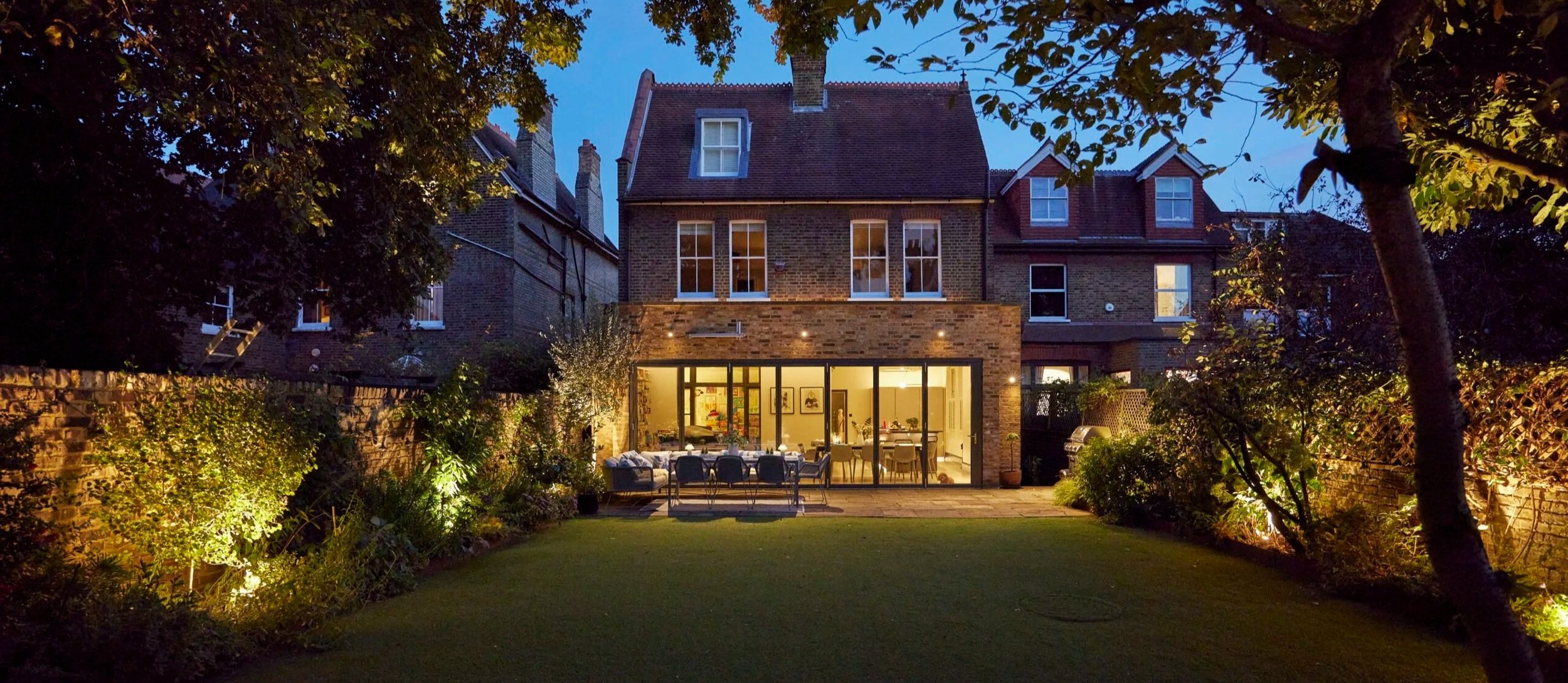 Evening view of a residential property with subtle exterior lighting highlighting the home and garden atmosphere.