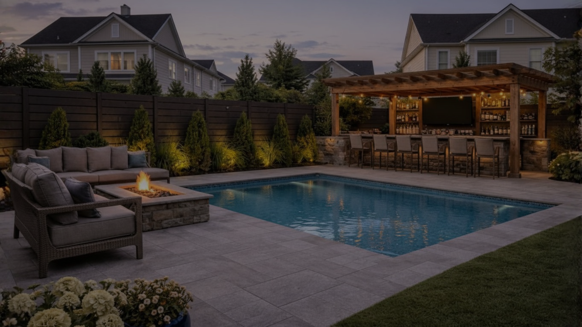 Private backyard with private swimming pool, outdoor seating with fire pit, landscaped plants, and a wooden outdoor bar with barstools at dusk.