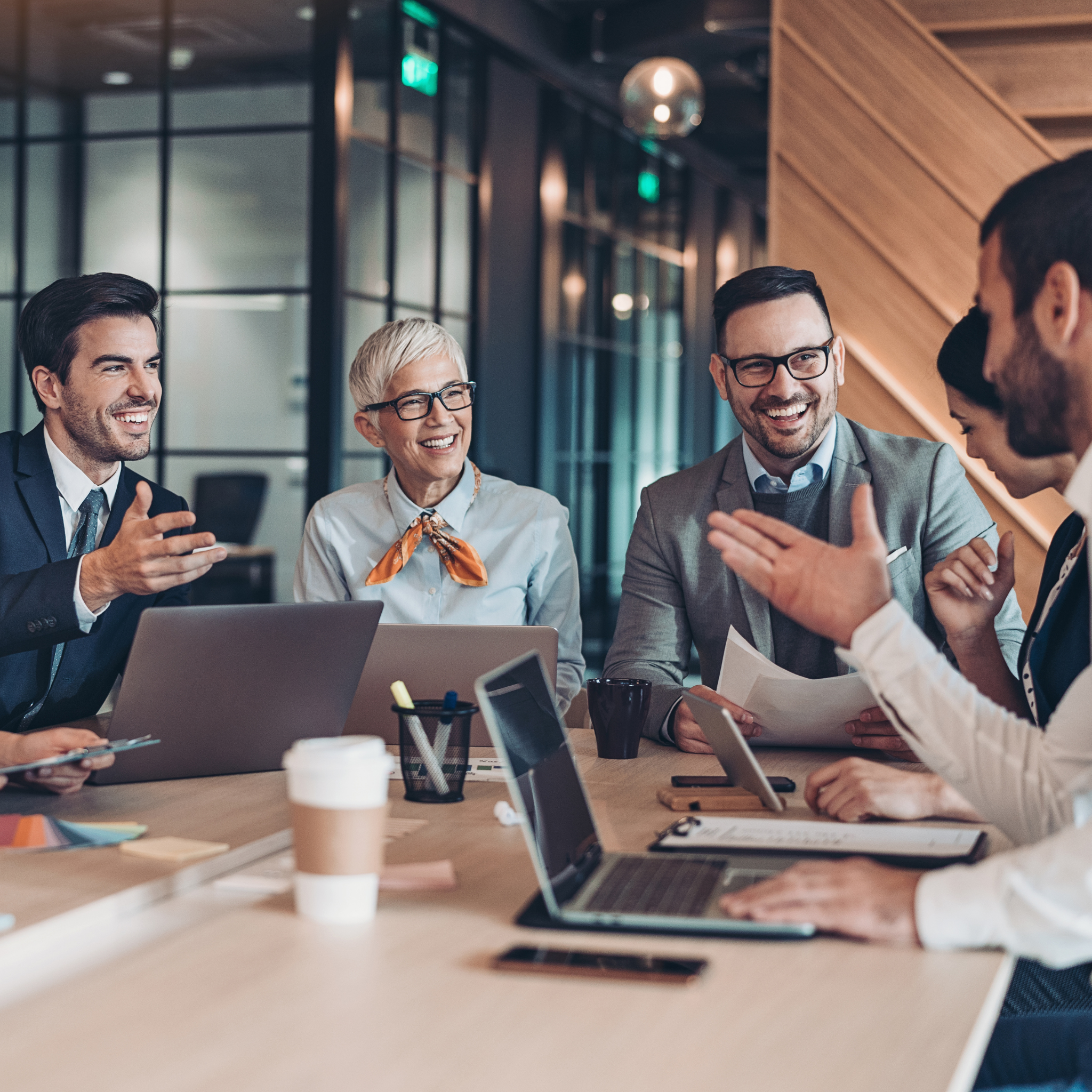 A group of five diverse professionals sitting around a conference table, engaged in a lively discussion and smiling.