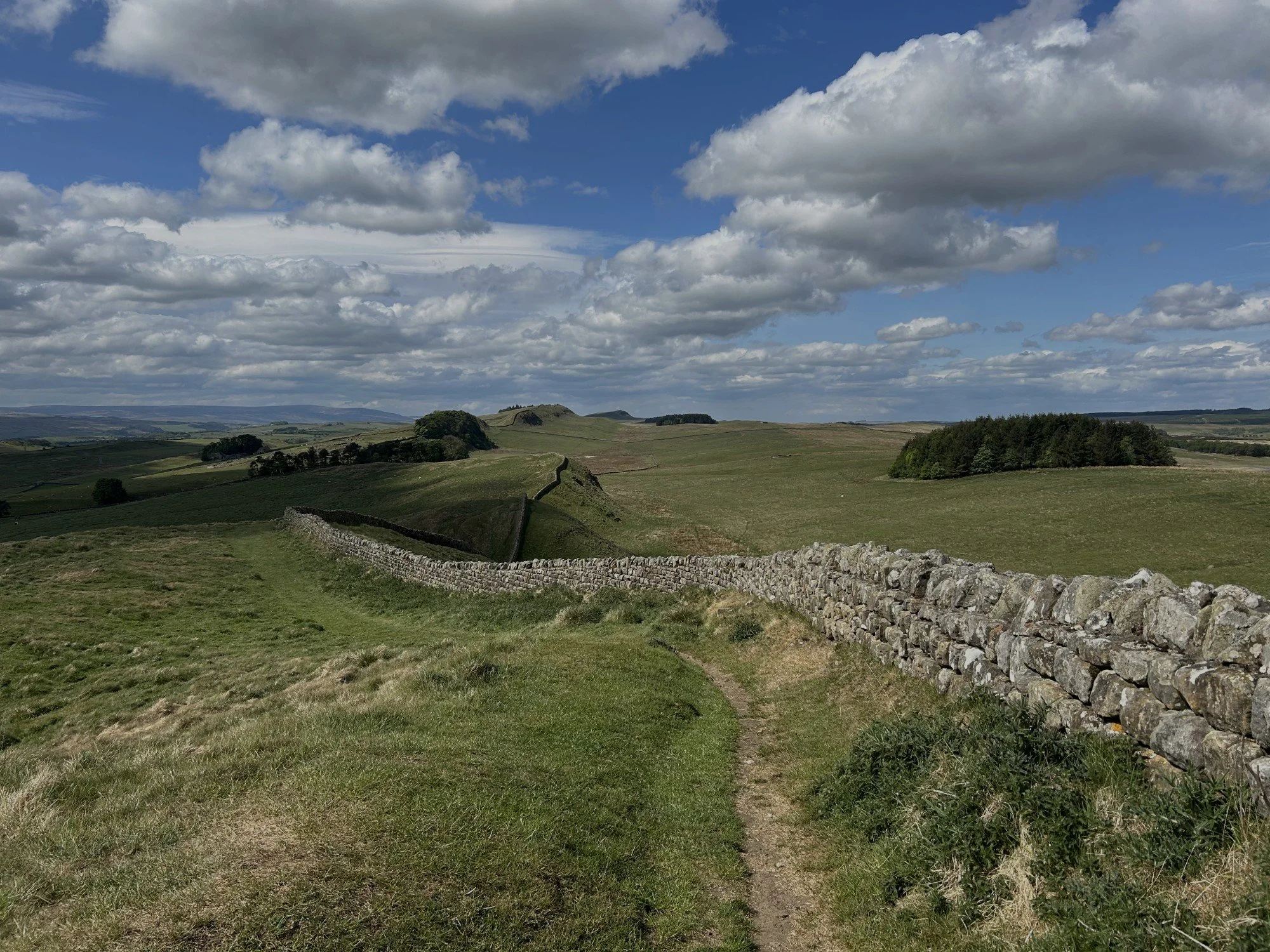 A stone wall running through rolling green hills under a partly cloudy sky.