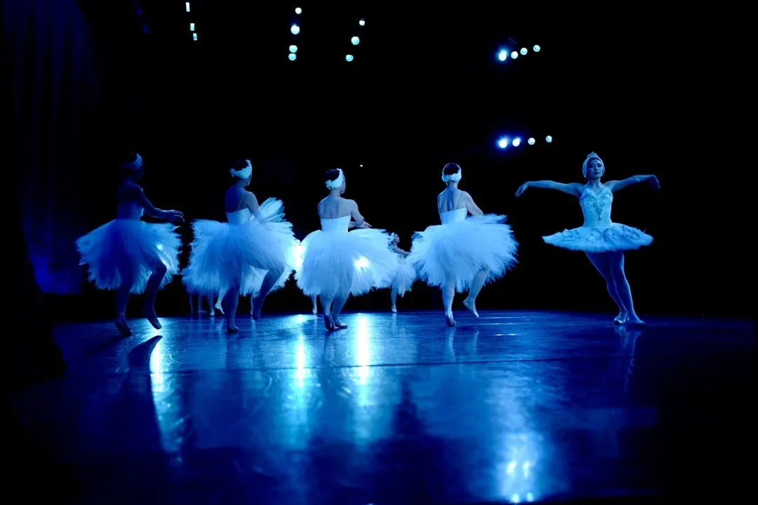 Ballet dancers in tutus performing on stage under blue lighting.
