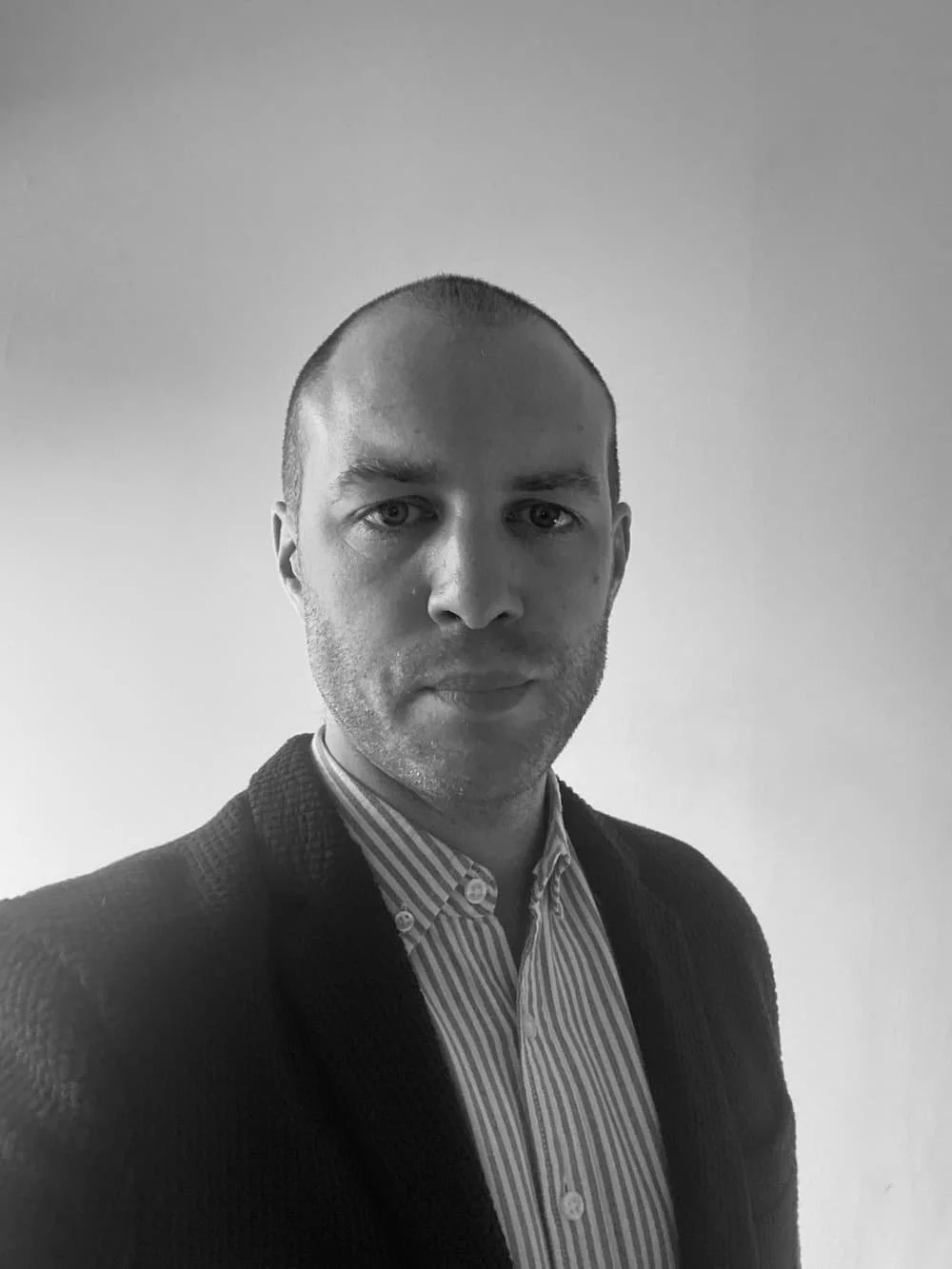 Black and white portrait of George William Flynn, contemporary garden designer, standing wearing a shirt and jacket