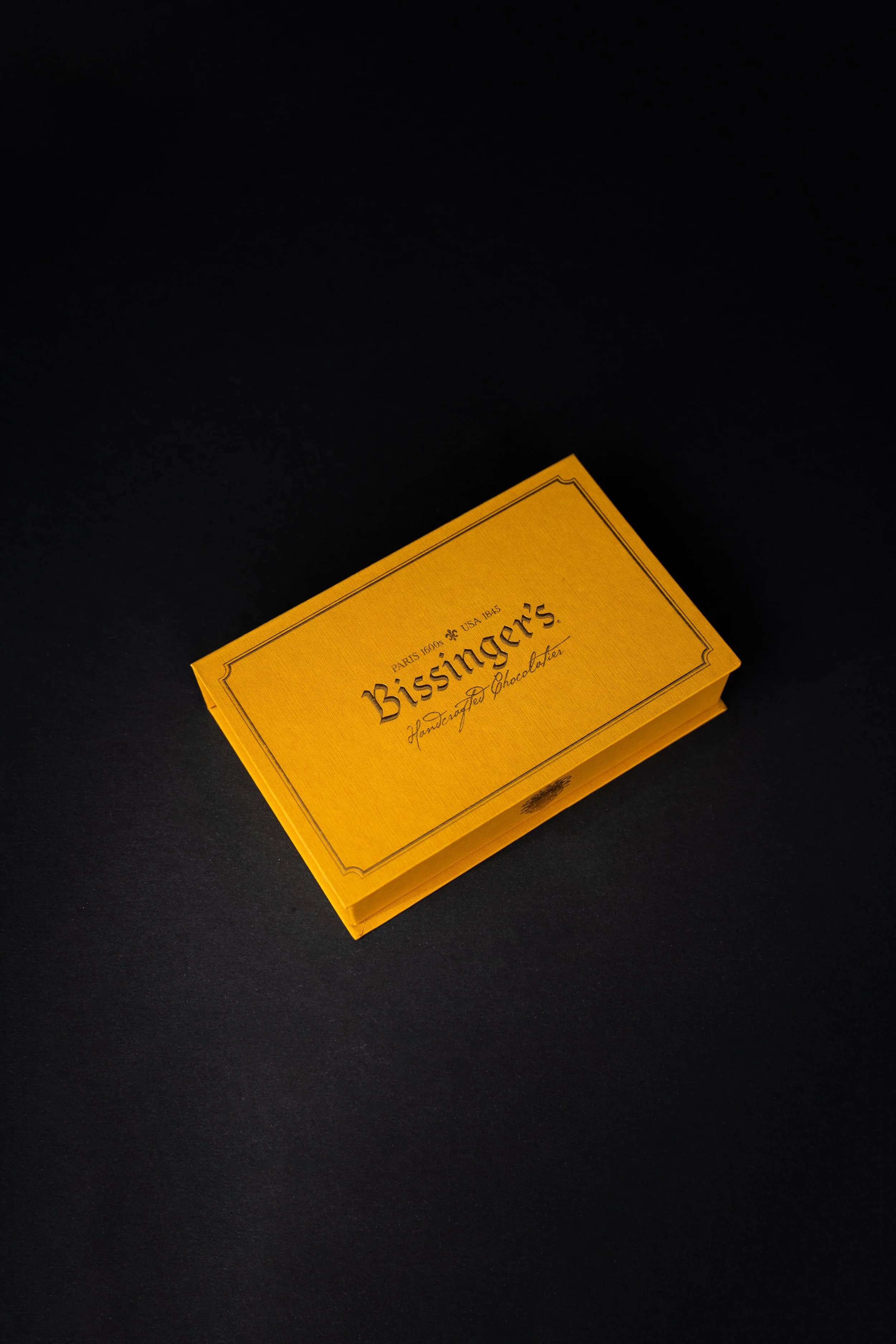 Yellow box of Bisinger's handcrafted dark chocolate on a white background.