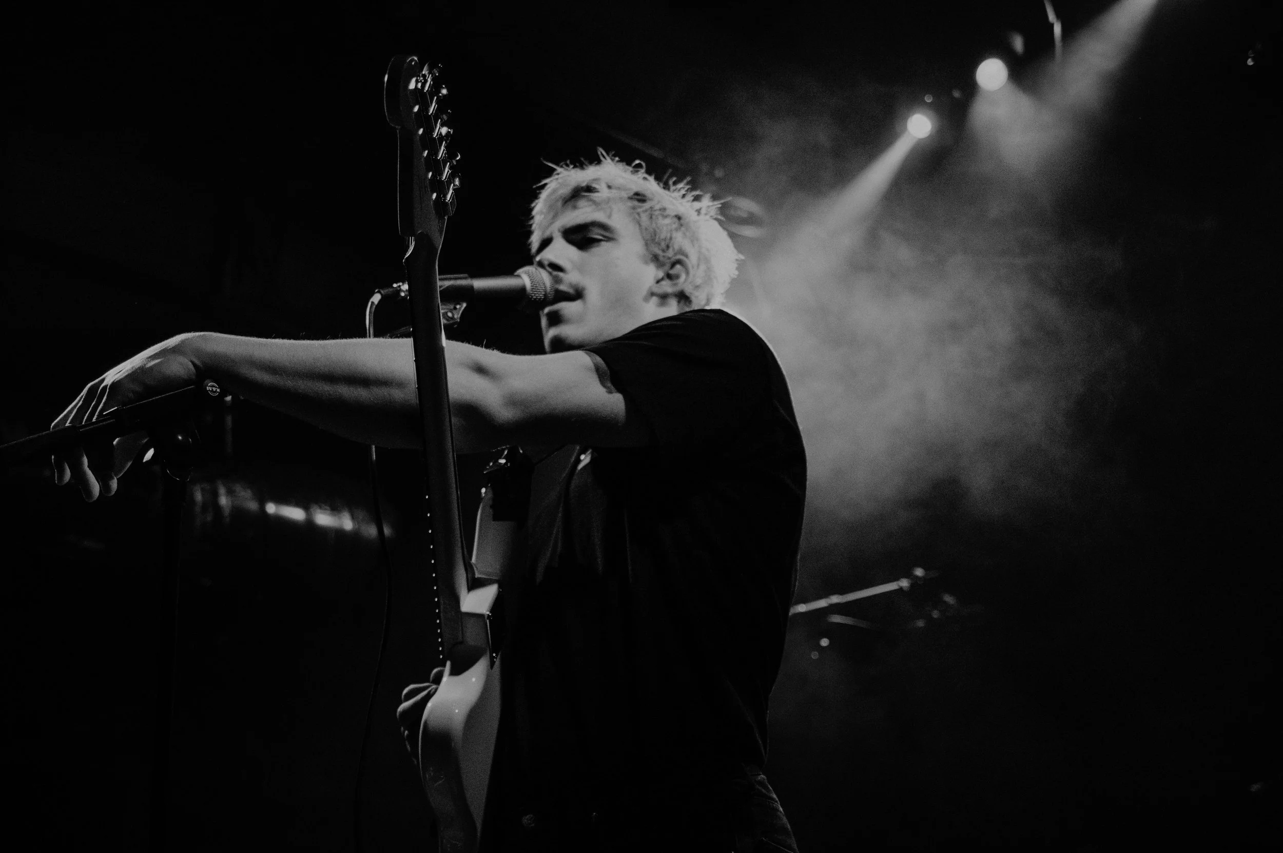 Musicien avec une guitare acoustique chantant dans un micro sur scène en noir et blanc.