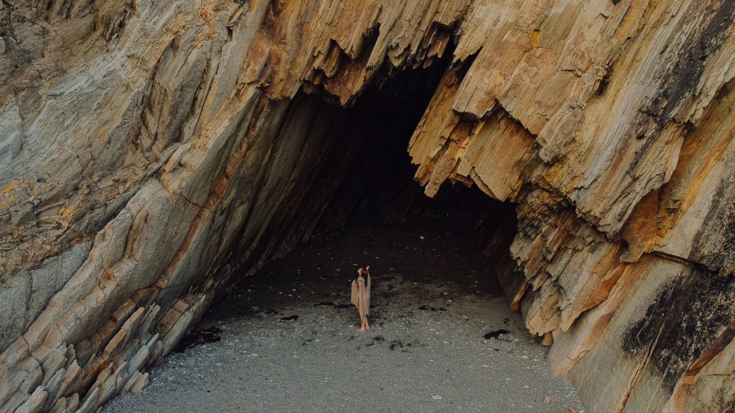 A person standing in a natural cave formation with rock walls and a sand floor, facing the camera.