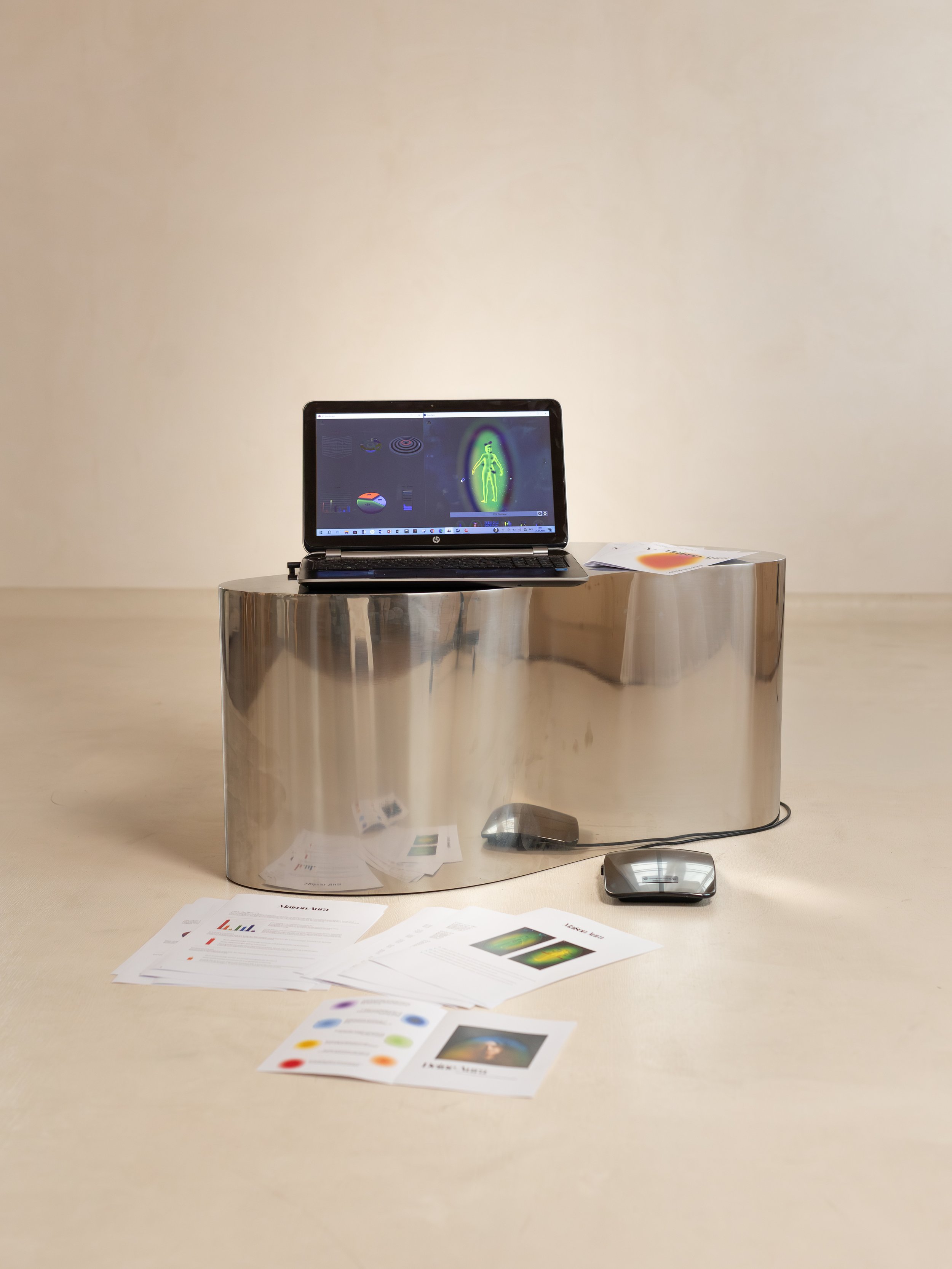 Ein Laptop auf einer reflektierenden, metallischen Ablage mit Diagrammen und Papieren, daneben ein Computermaus, im Hintergrund eine beige Wand.