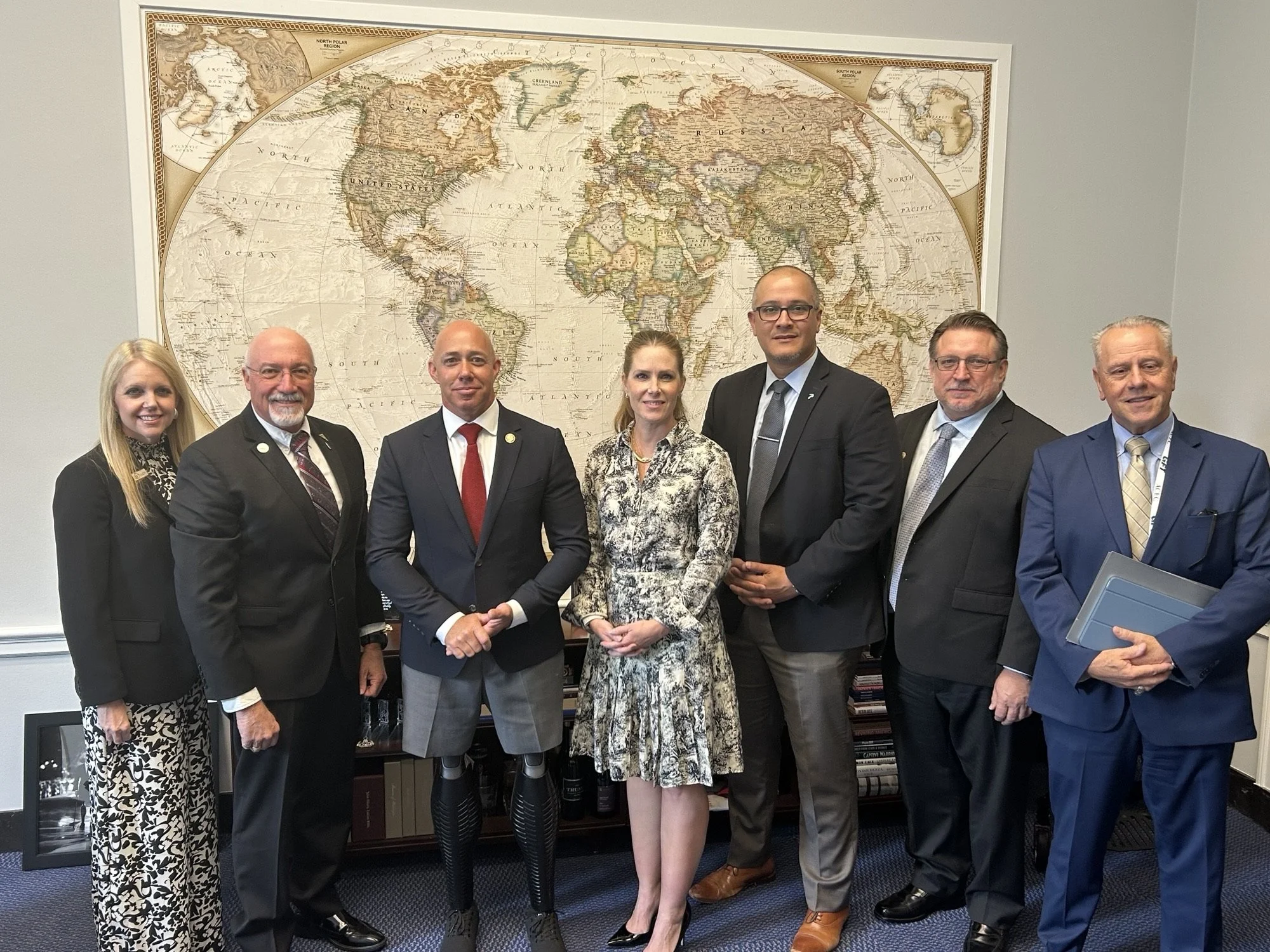 Group of seven professionally dressed people standing in front of a world map in a conference room.
