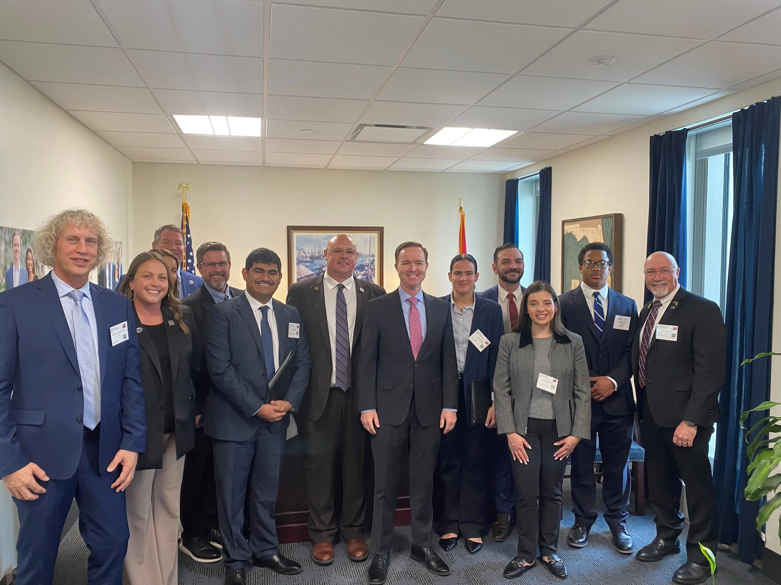Group of professionals standing together in a conference room, dressed in business attire, smiling at the camera.