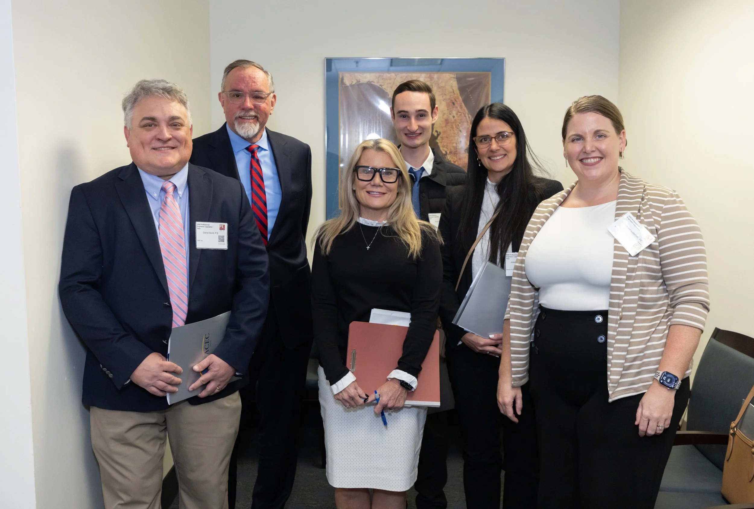 Group of seven professionals at a formal event, standing together and smiling for the photo, with some holding notebooks and folders.