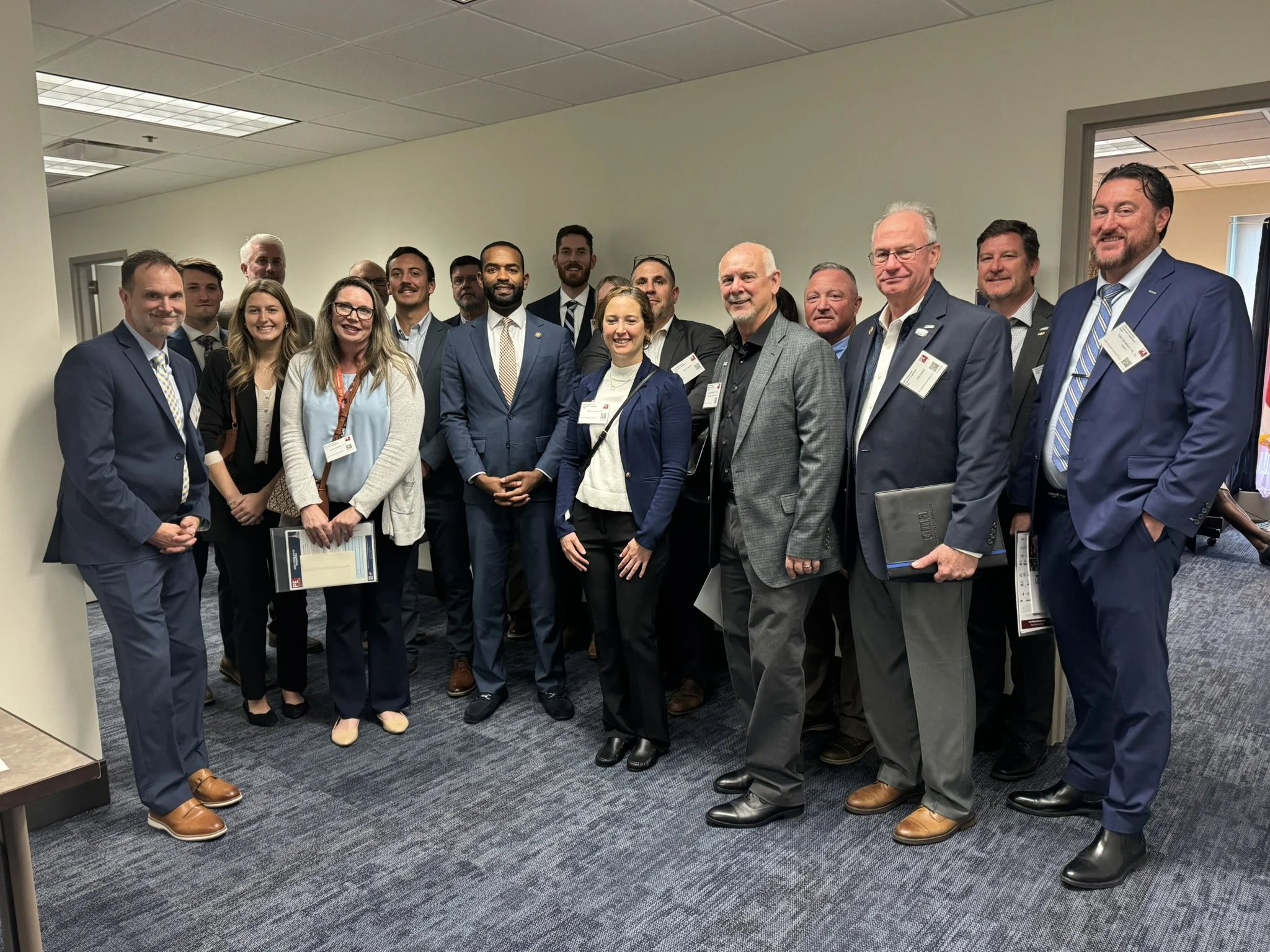 Group of professionals in business attire posing for a photo in an office corridor.