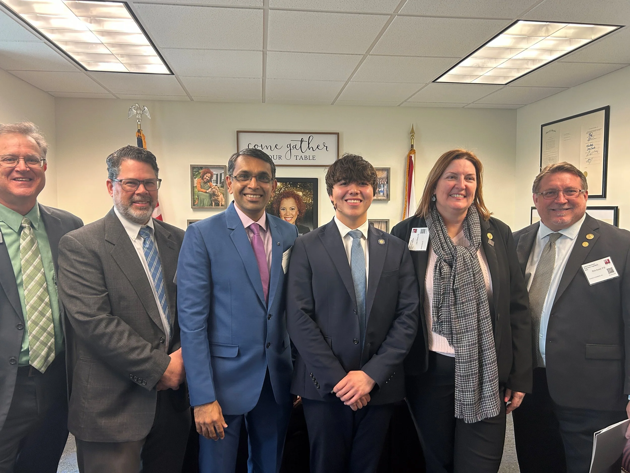 Group of seven professionally dressed individuals standing in a conference room, smiling at the camera.