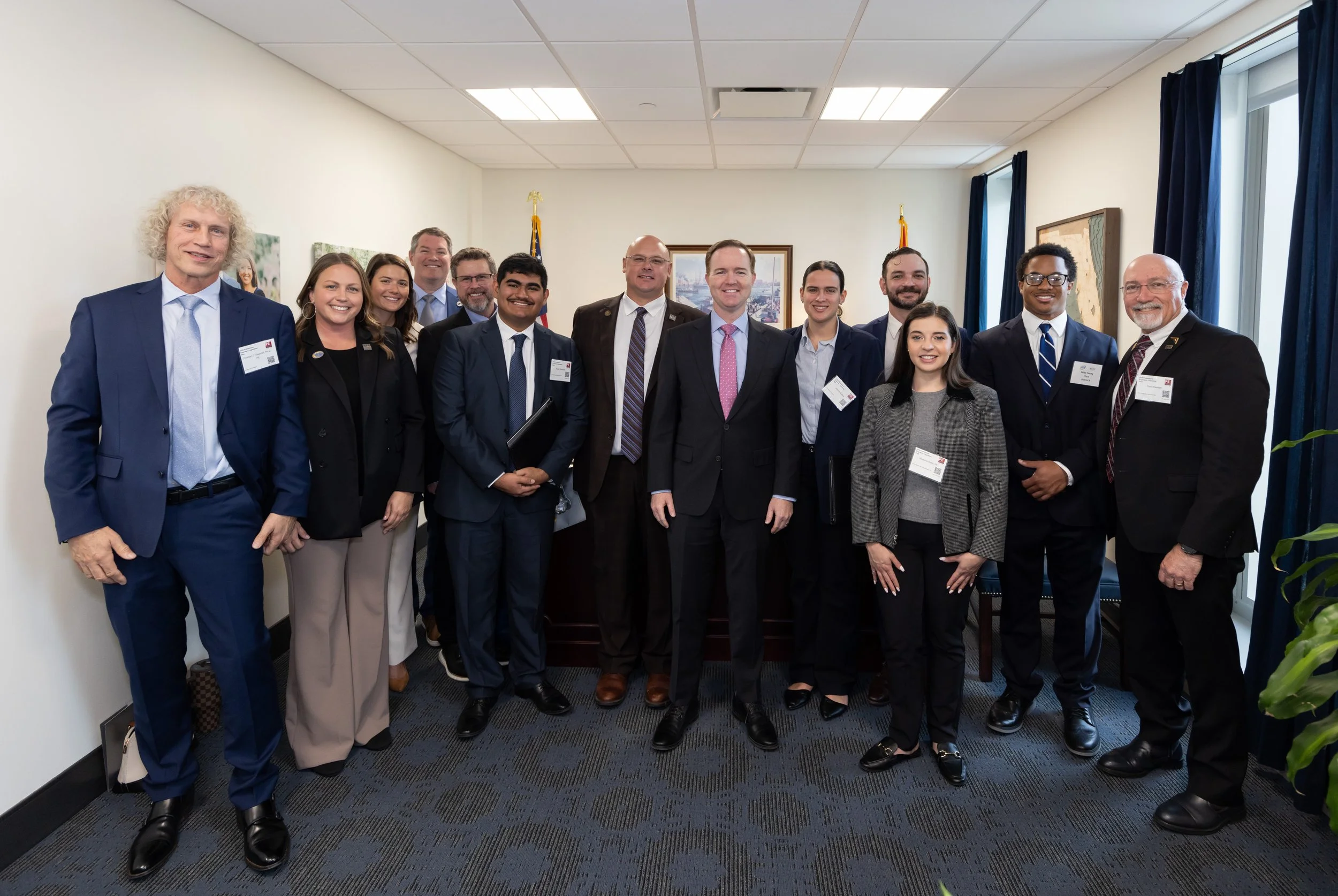Group of diverse professionally dressed people standing in a conference room, posing for a group photo.