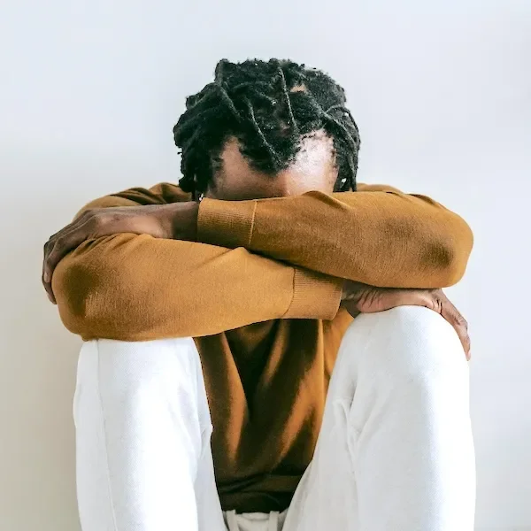 man sitting with forehead resting on crossed arms