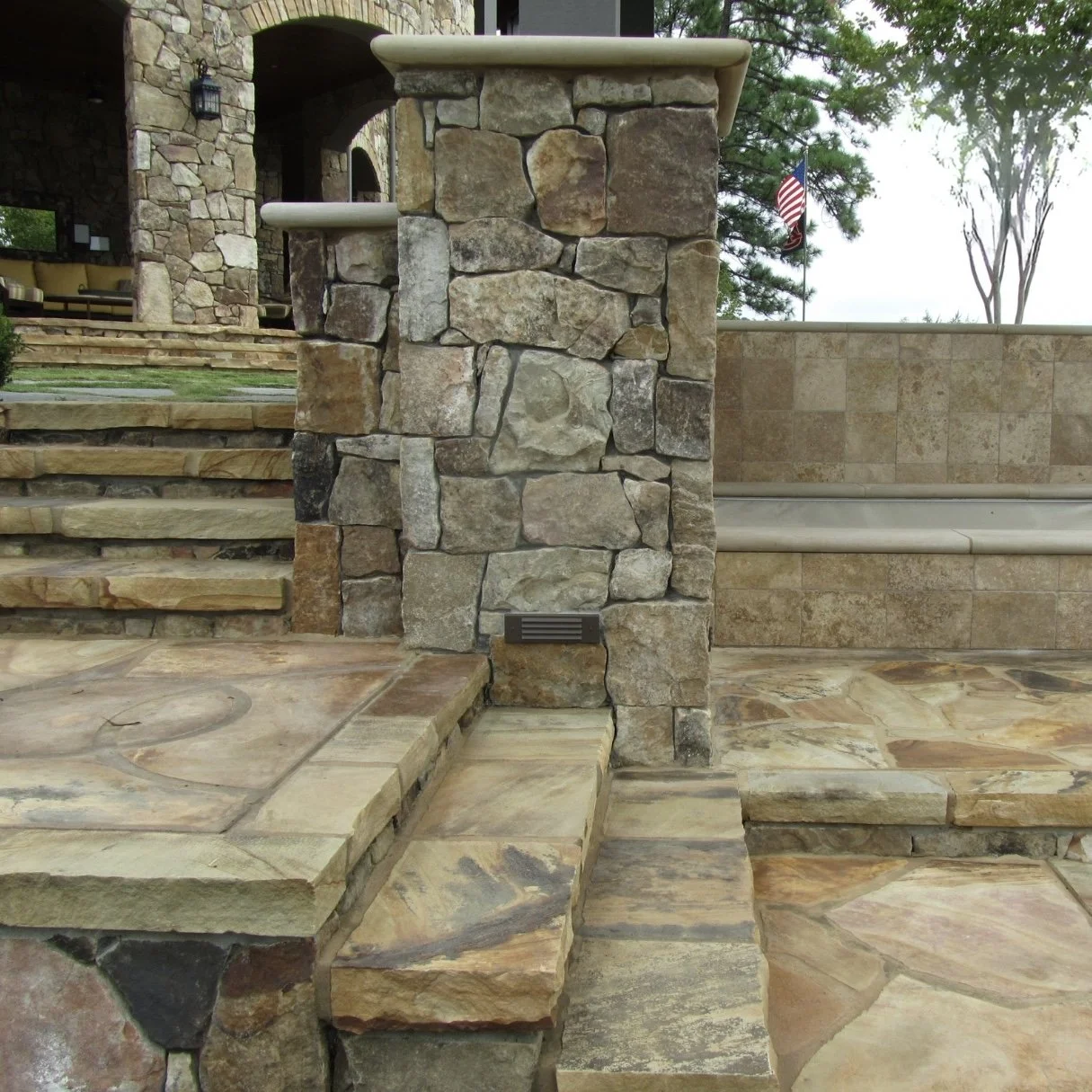Stone and tile outdoor steps and wall by Iron City Retaining Walls, a retaining wall builder in Central Alabama, with an American flag in the background.