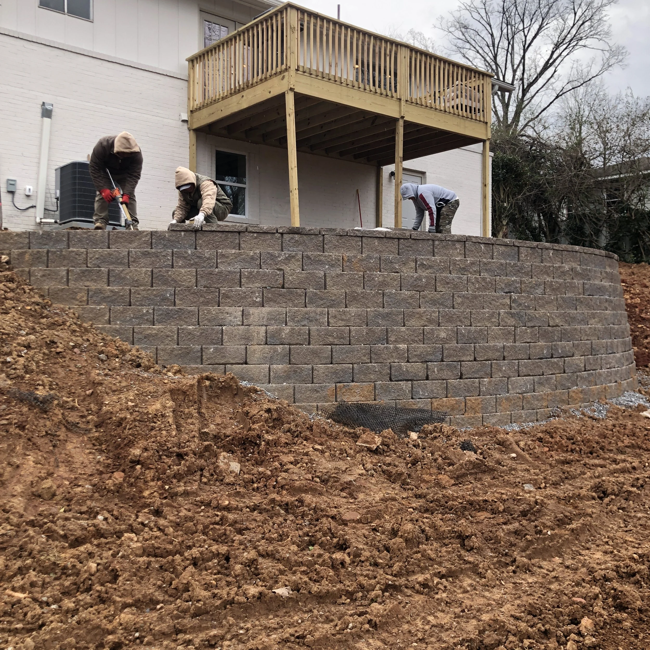 Commercial retaining wall contractors with Iron City Retaining Wall's image showing three workers building a block retaining wall for a building.