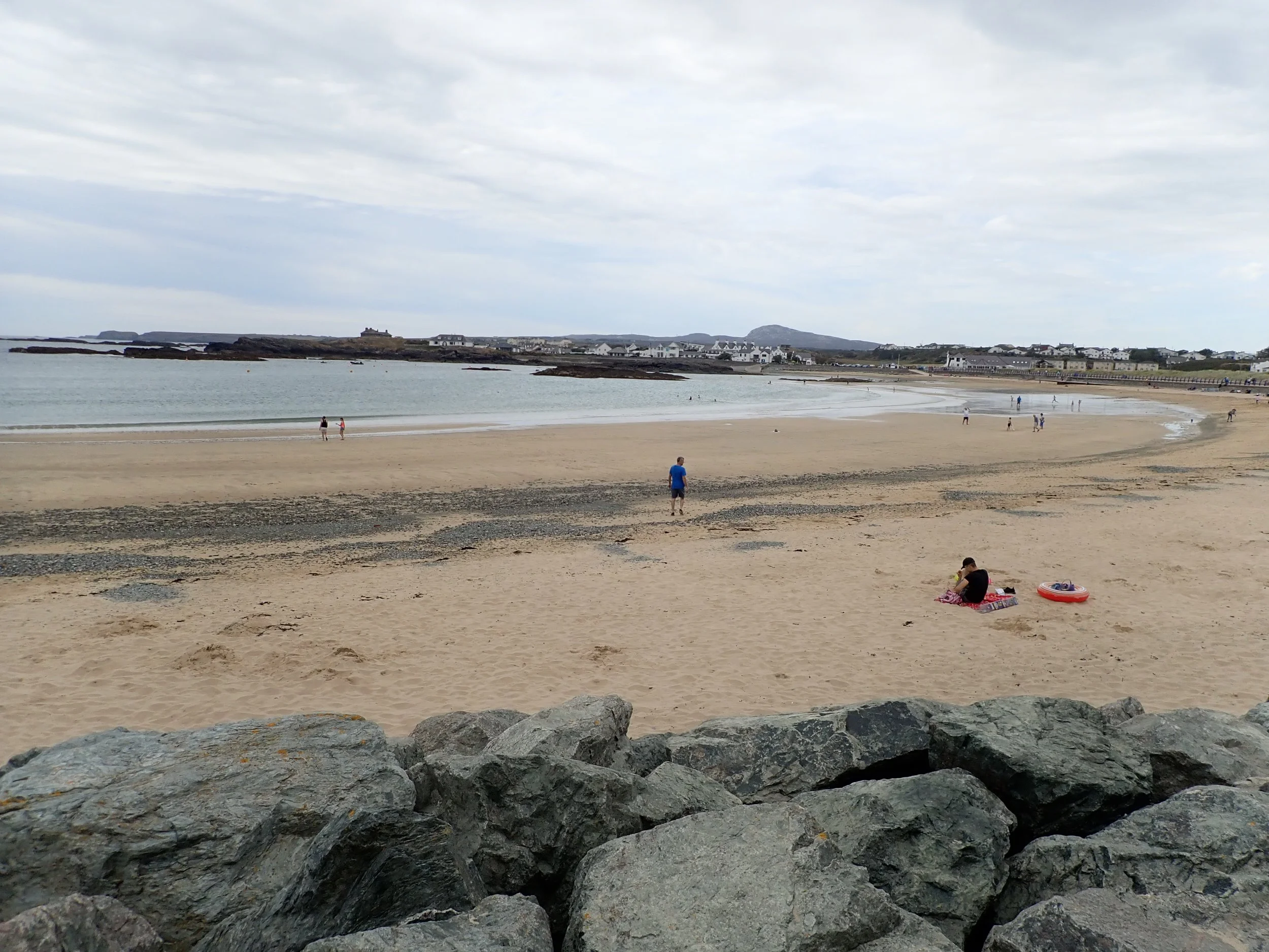A sandy beach curving round a bay, with rocks in the foreground