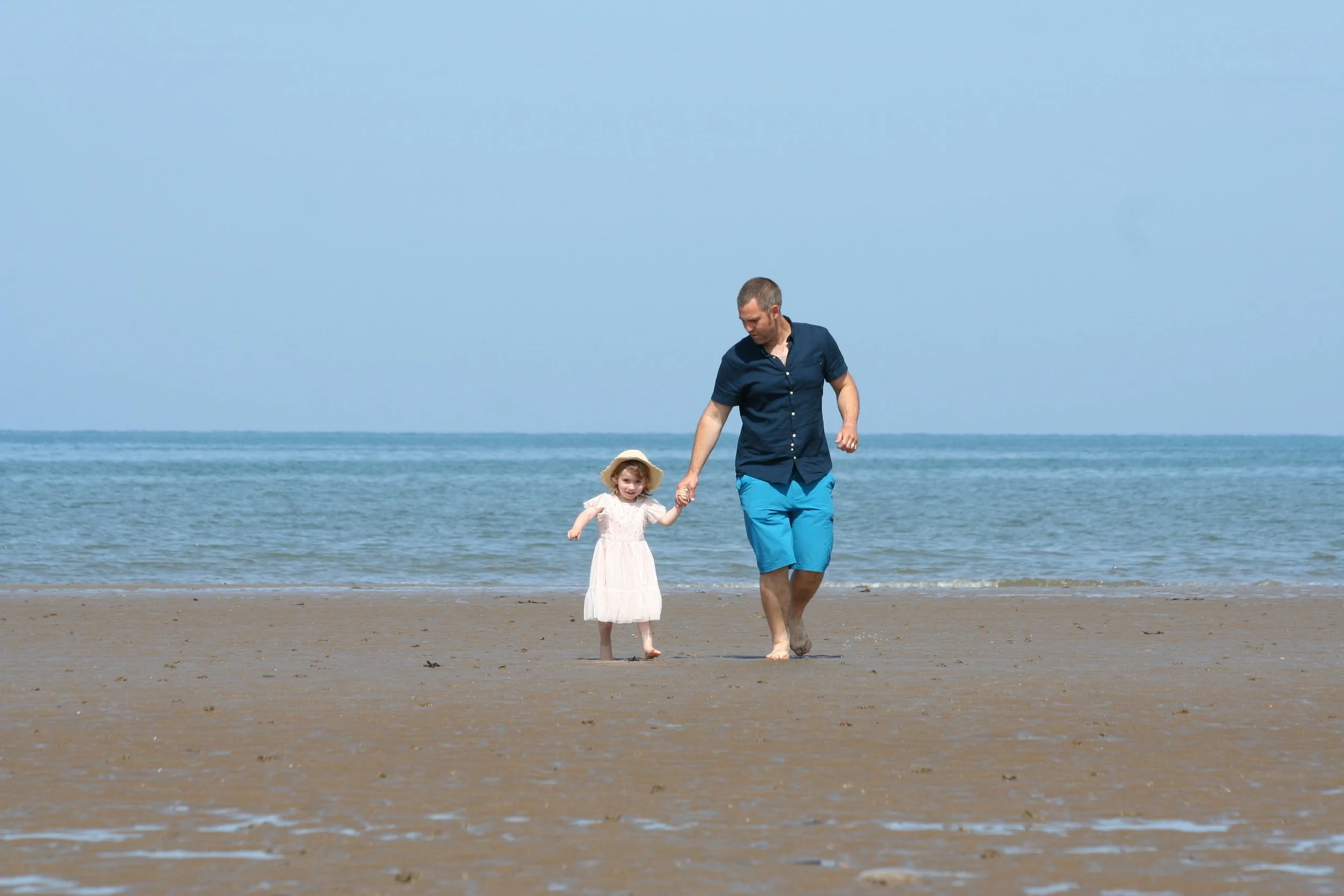 A man and a toddler walking together along a sandy beach