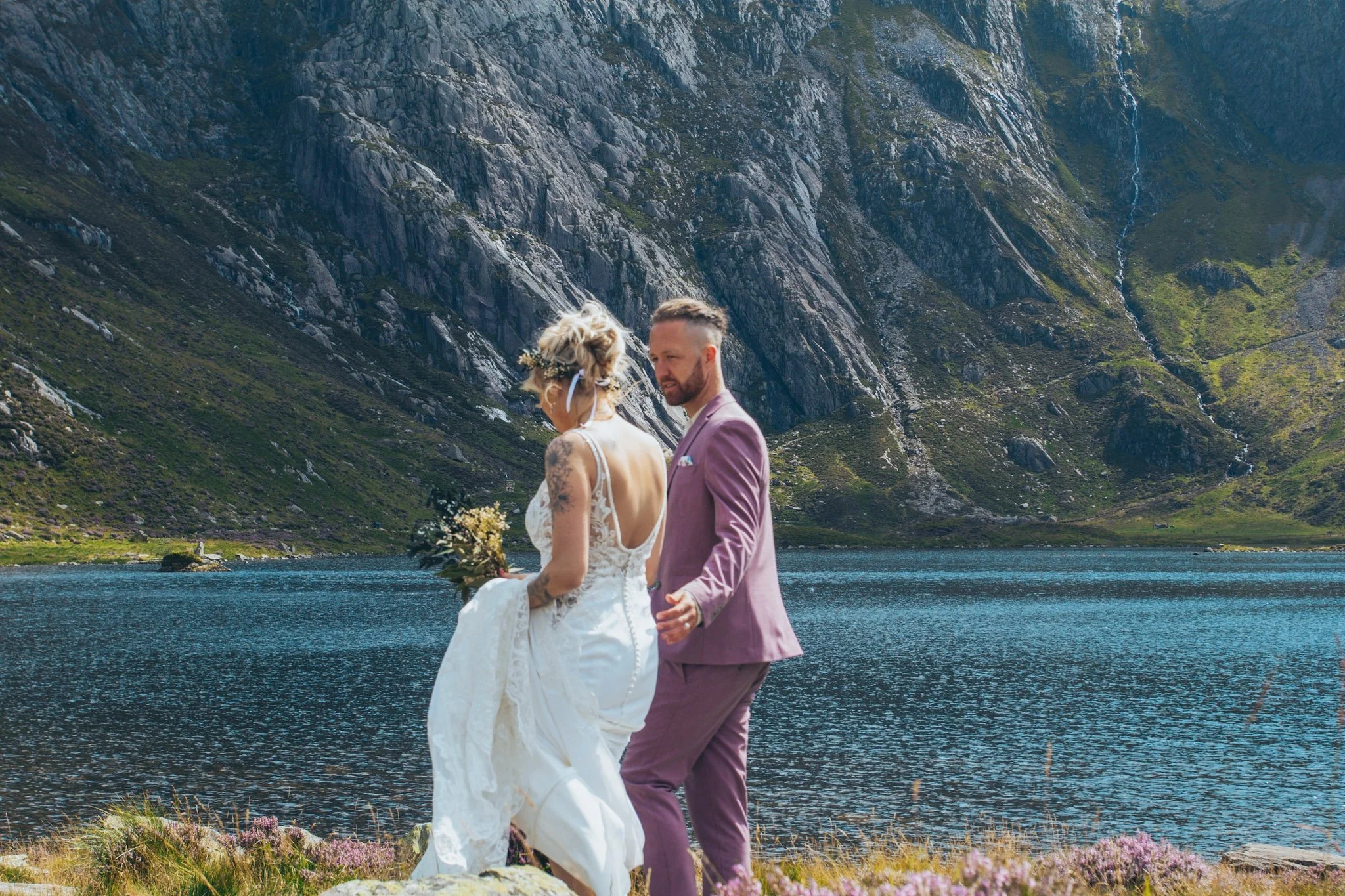 A couple standing on a lakeshore beneath a mountain