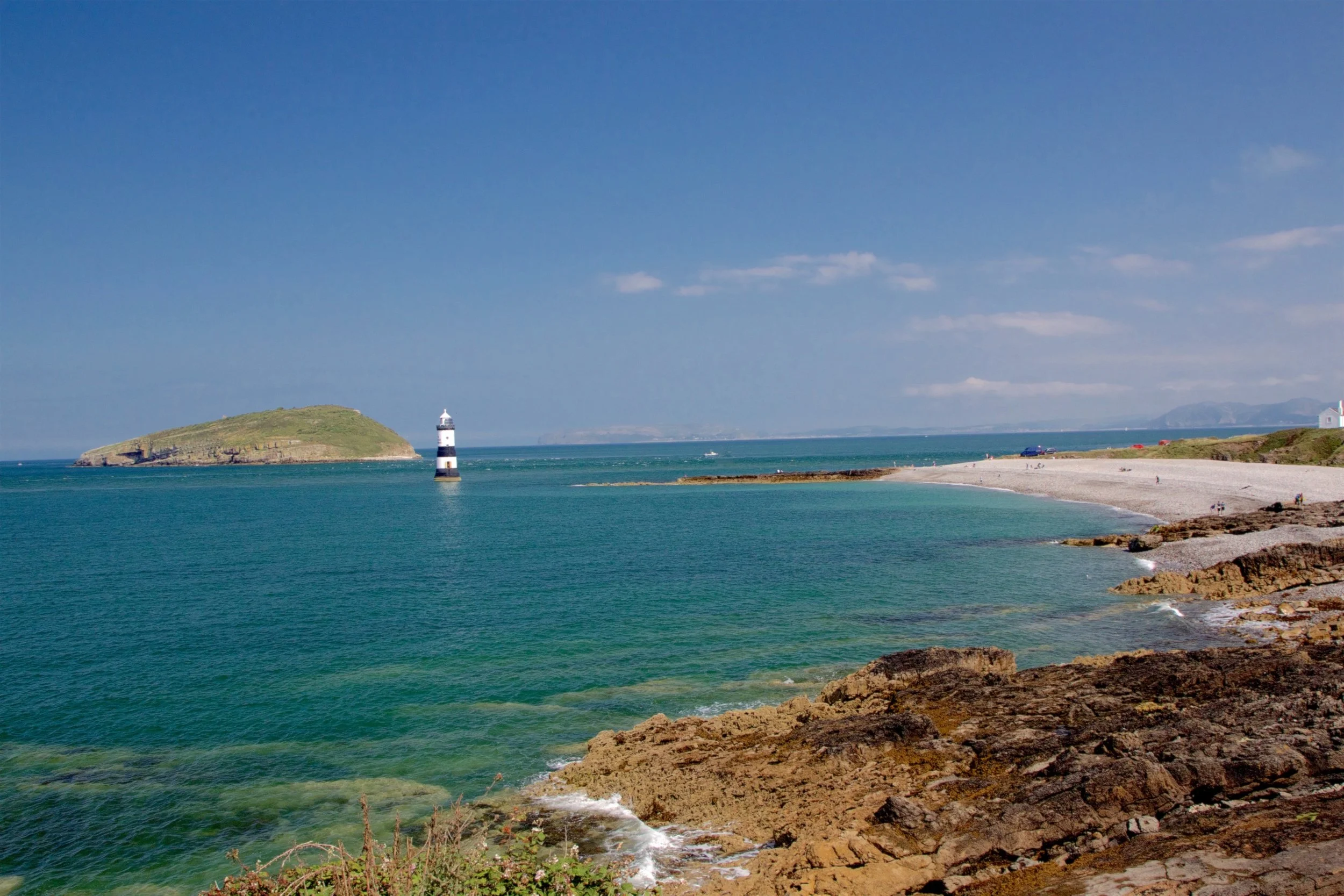 Trwyn Du lighthouse at Penmon Point, with Puffin Island and clear turquoise water on a sunny day