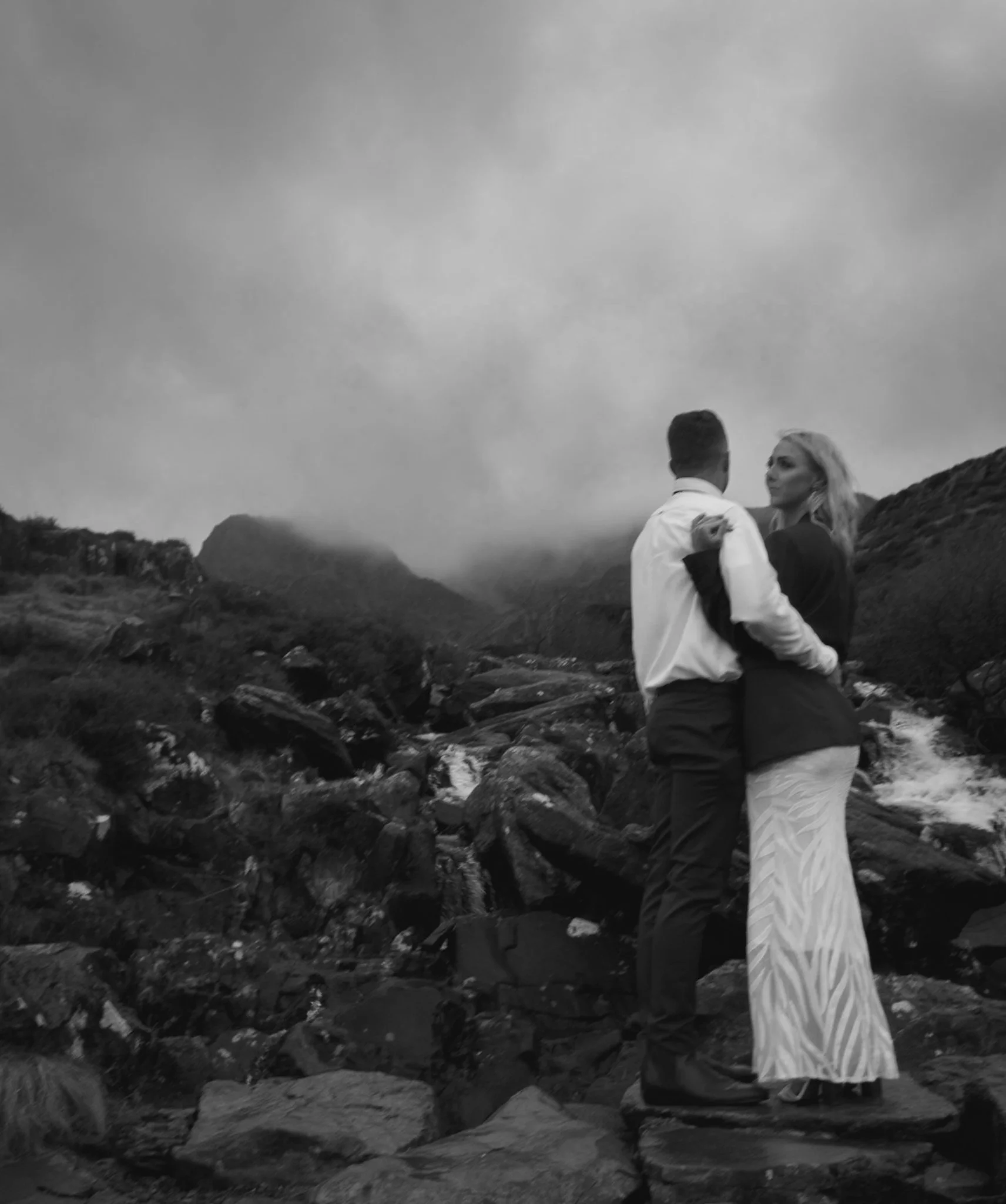 A couple embracing on rocks beside a waterfall, in black and white