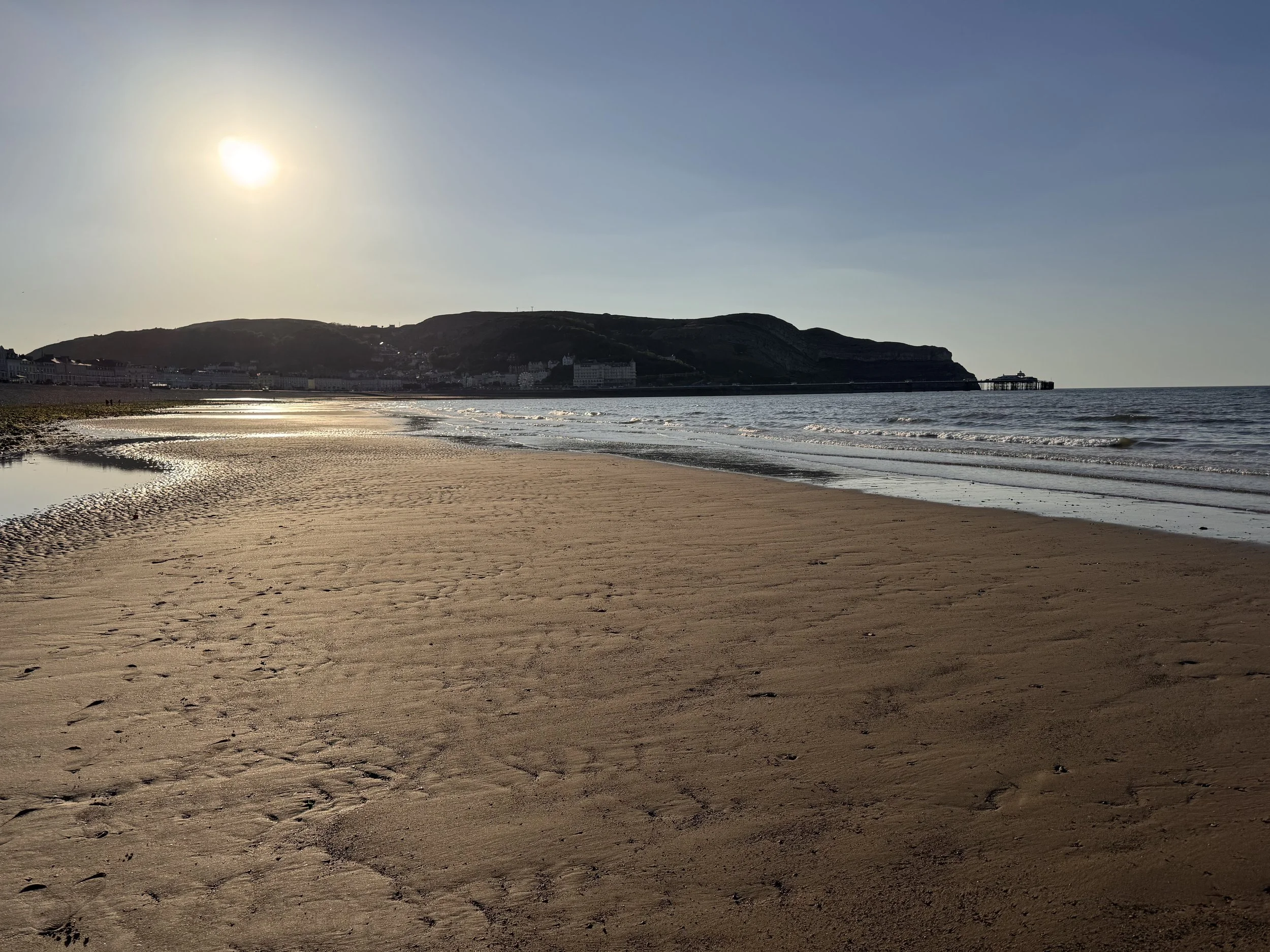 A wide sandy beach at low tide with a headland in the distance