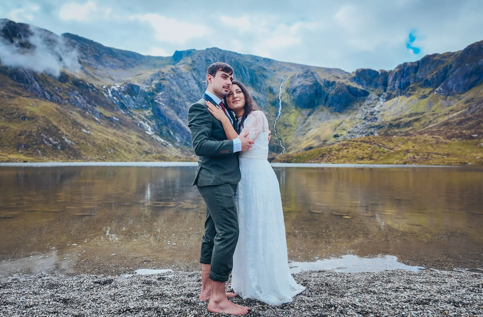A couple embracing barefoot on the shore of a mountain lake