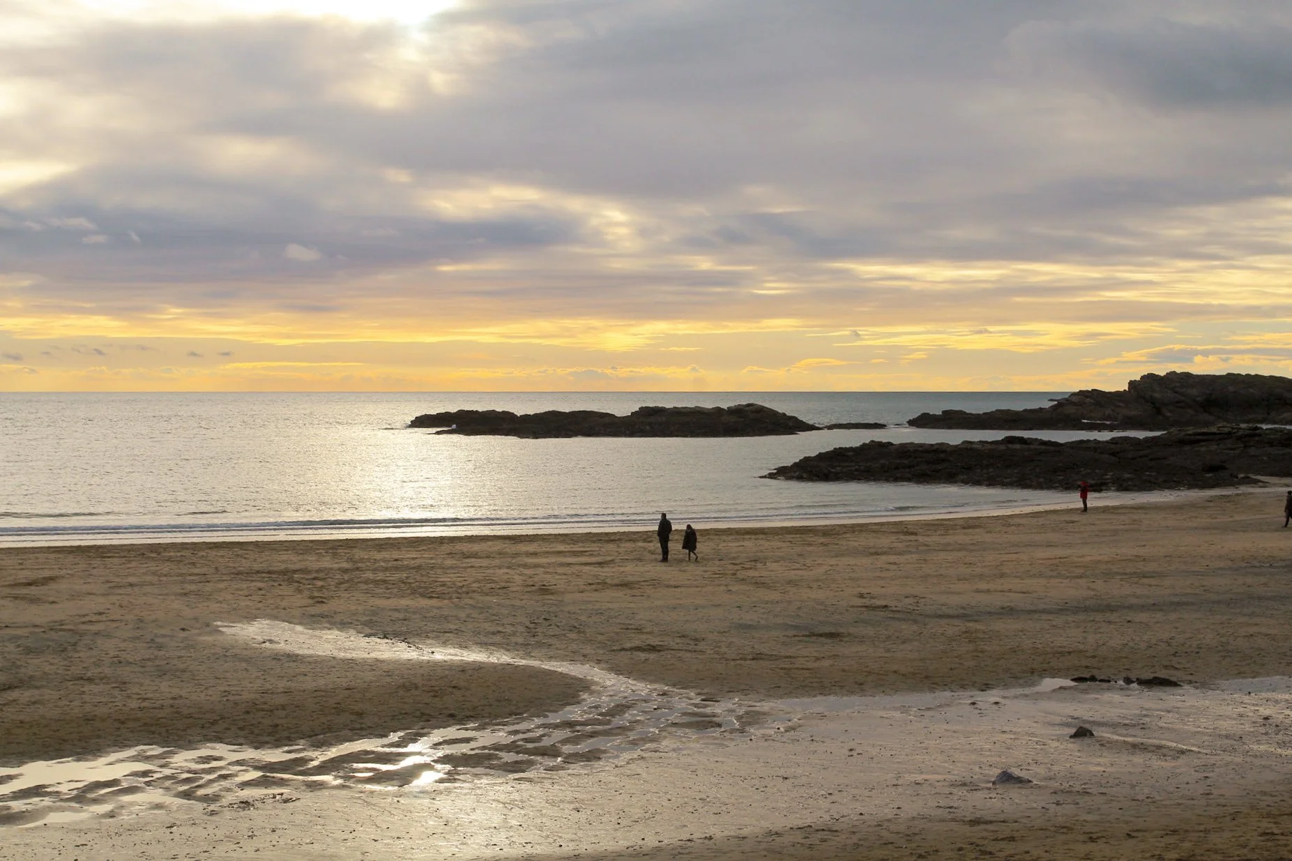 A sandy beach at sunset with two people walking in the distance