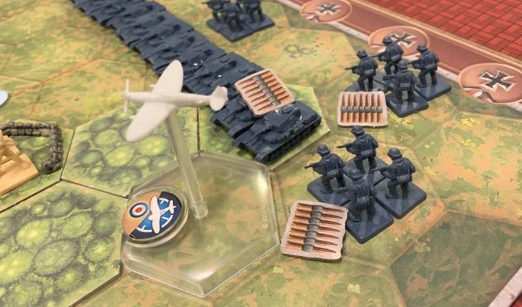 Tabletop war game with miniature soldiers, tanks, and an aircraft on a hexagonal grid map.