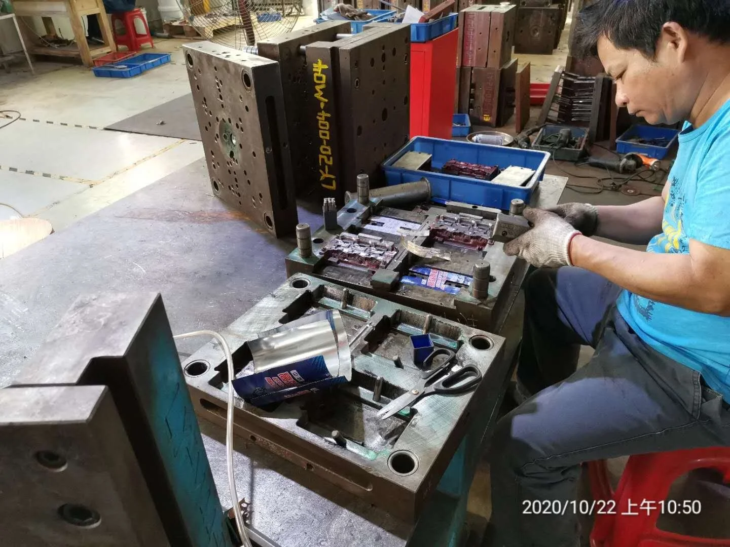 A man working on a machine at a workbench in a workshop with tools and parts around.