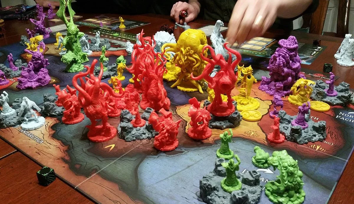 Colorful game pieces on a board game map, with players' hands reaching in to move pieces.
