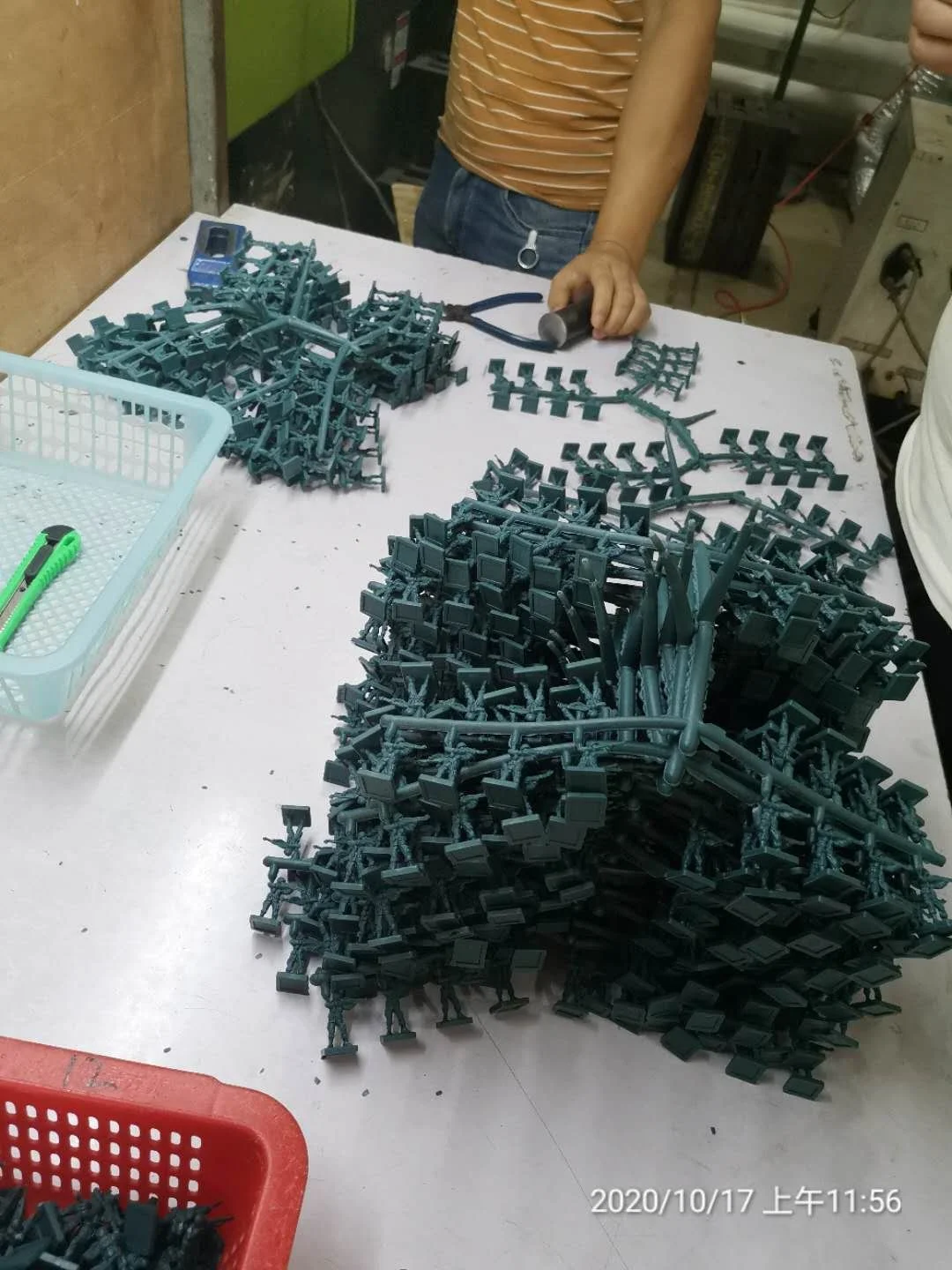 A person working on assembling small plastic model figures or objects on a white table, with scattered green plastic pieces and tools.