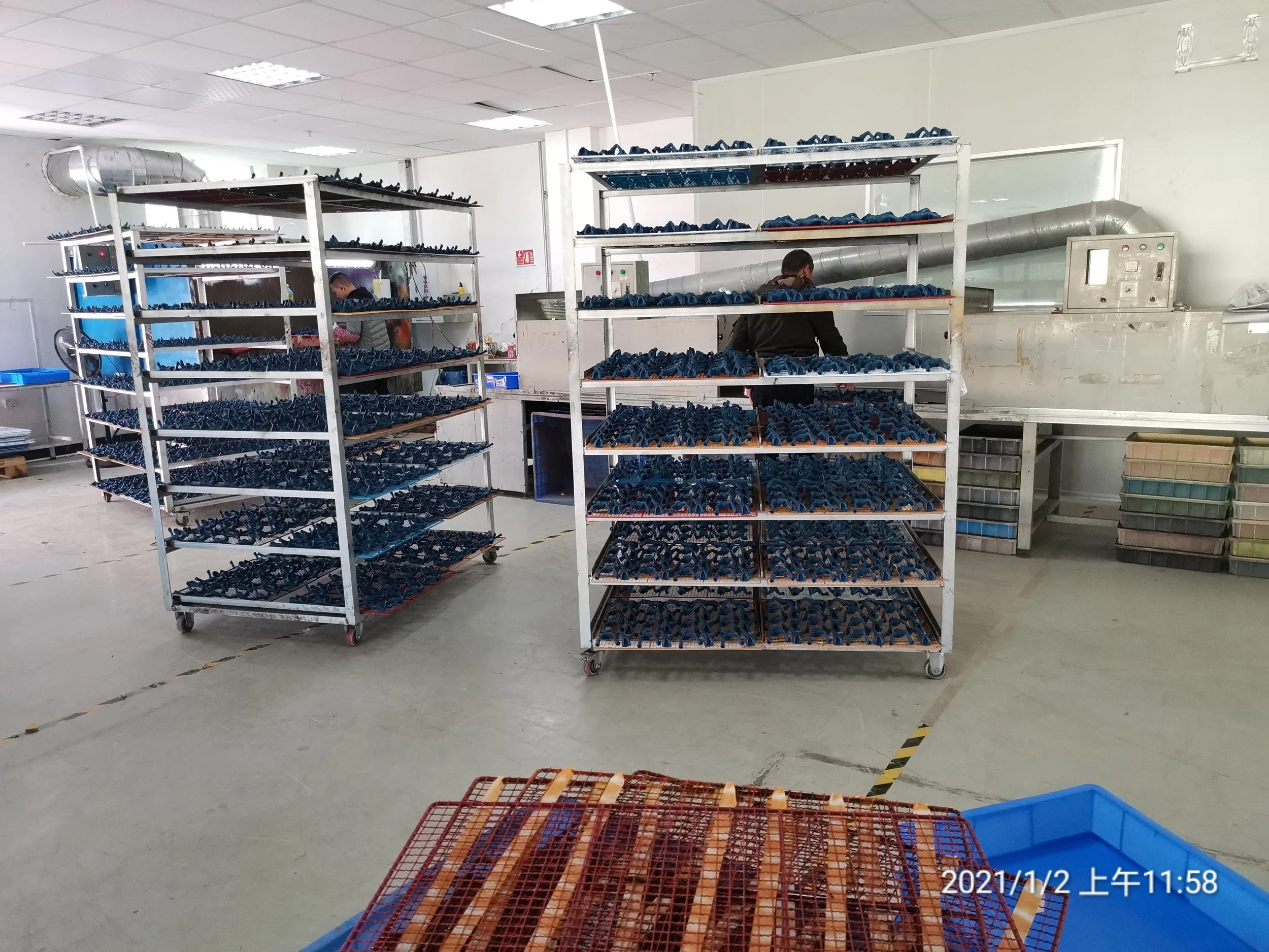 Industrial workspace with metal racks holding blue shoe soles and workers in background.