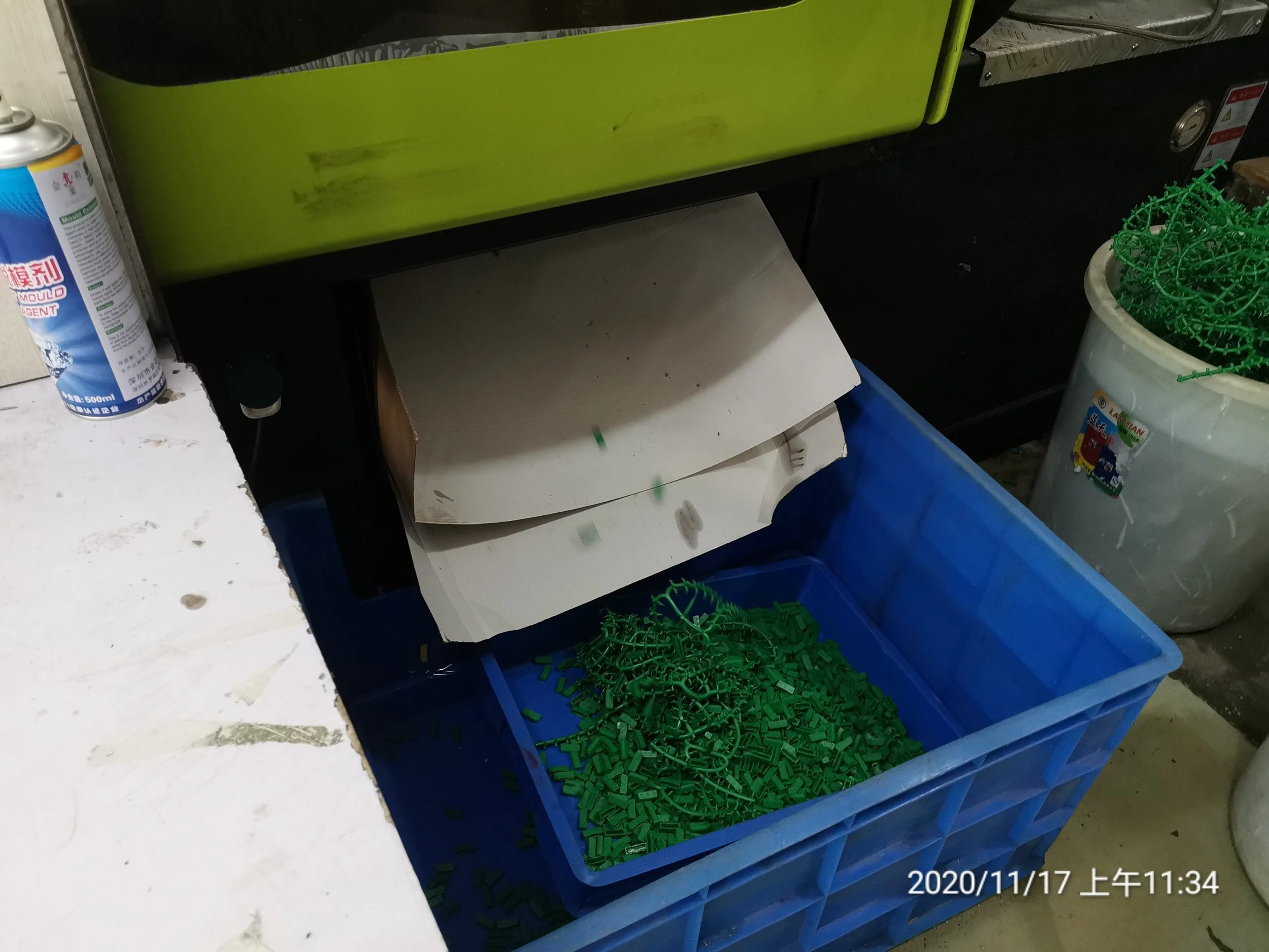 Blue plastic bin filled with green plastic cable ties in a workshop or storage area.