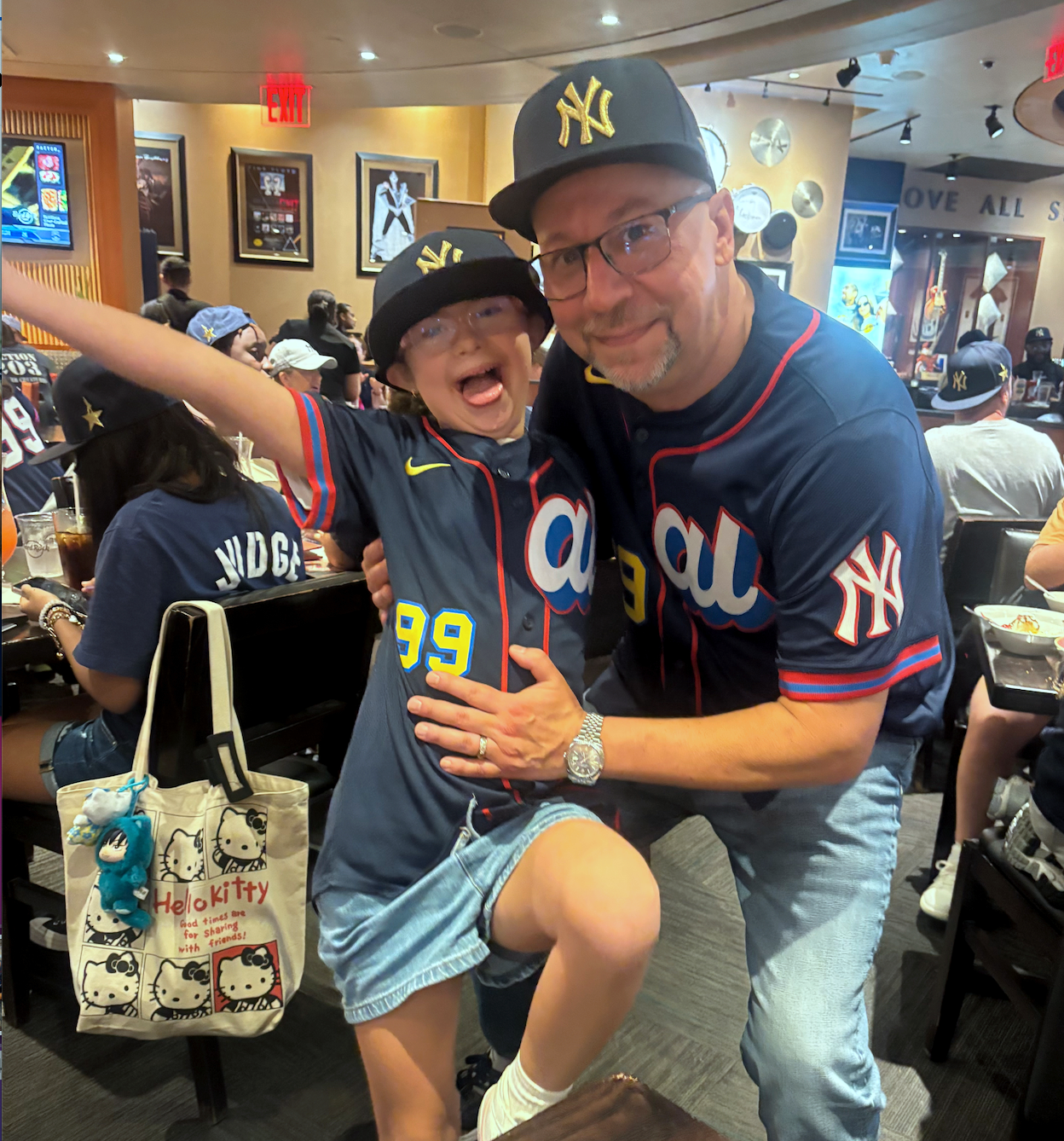A man and a boy wearing New York Yankees baseball jerseys and hats celebrating inside a restaurant or sports bar.