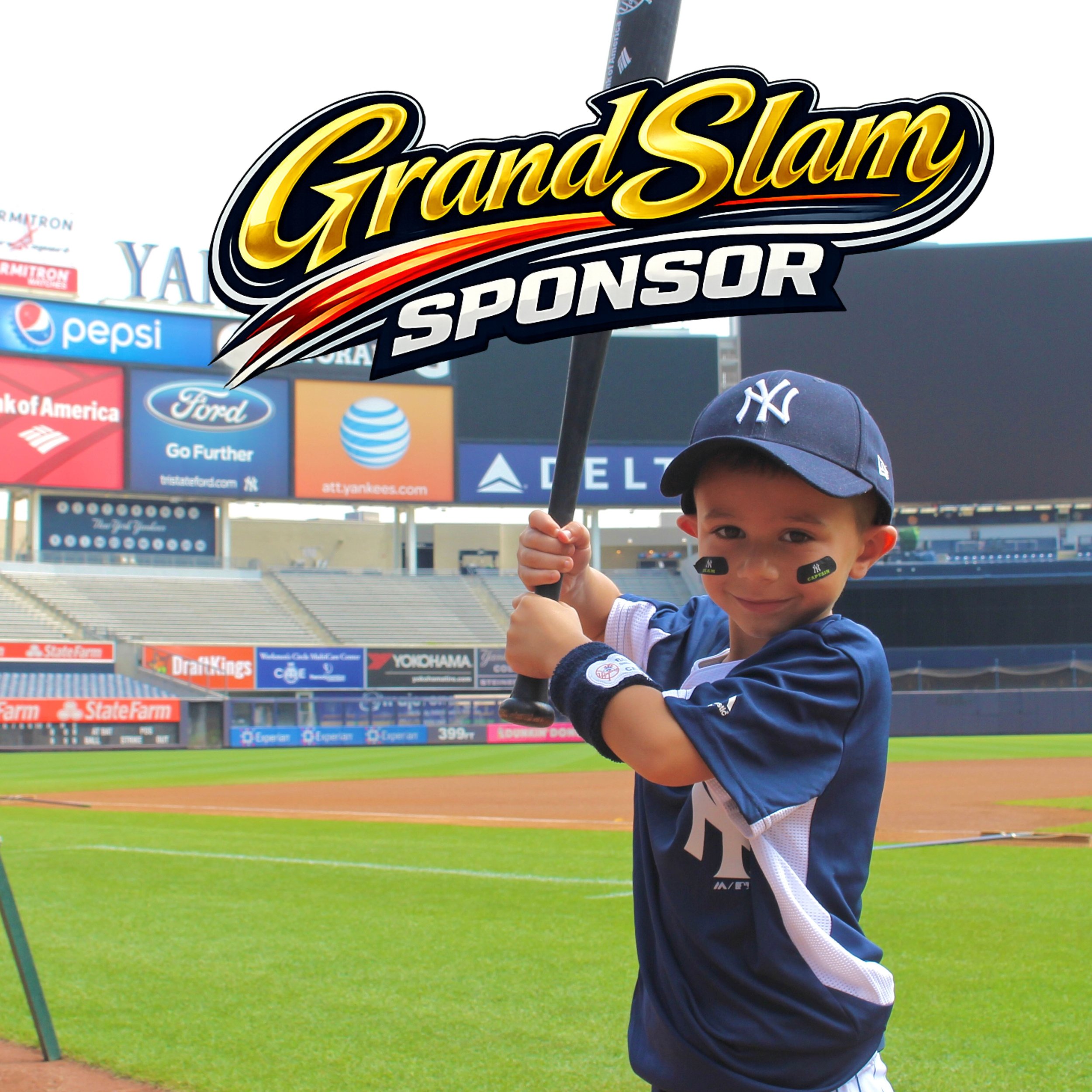 A young boy wearing a navy blue New York Yankees baseball cap and jersey, holding a bat at a baseball stadium with a large 'Grand Slam Sponsor' sign overhead, empty seats, and advertising billboards in the background.