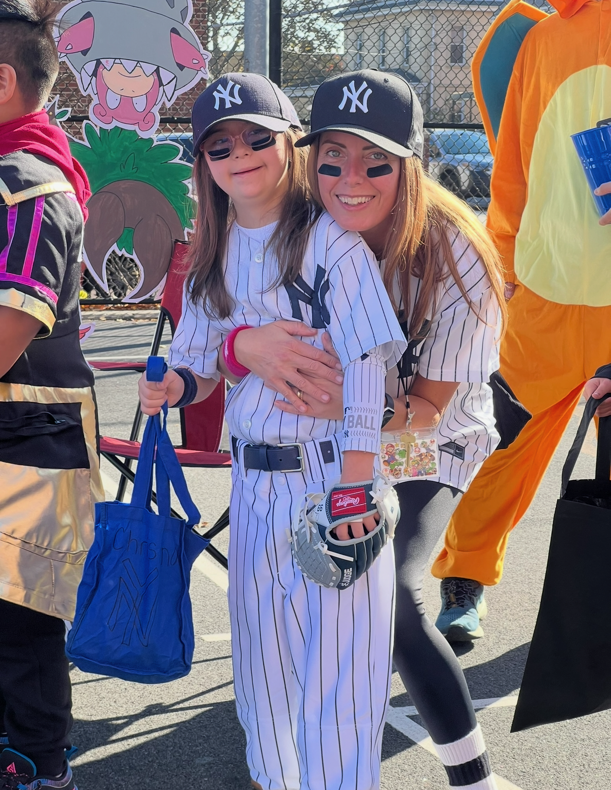 A woman and a young girl dressed in New York Yankees baseball uniforms at a themed event, hugging and smiling for the camera.