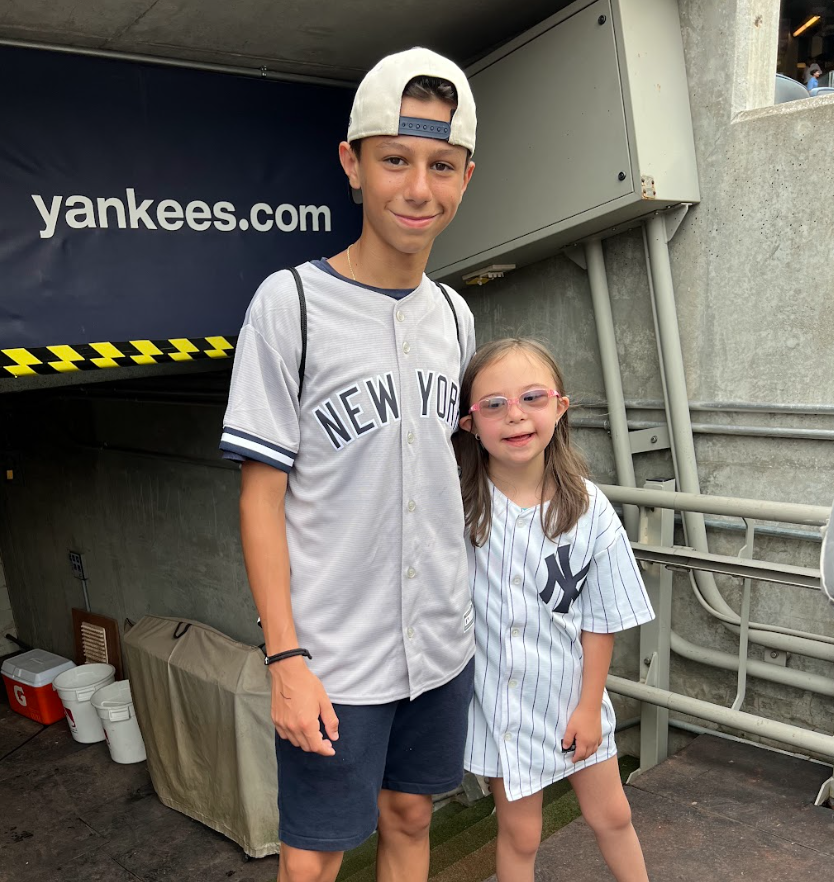 A teenage boy and a young girl wearing New York Yankees baseball jerseys, standing side by side and smiling outdoors.