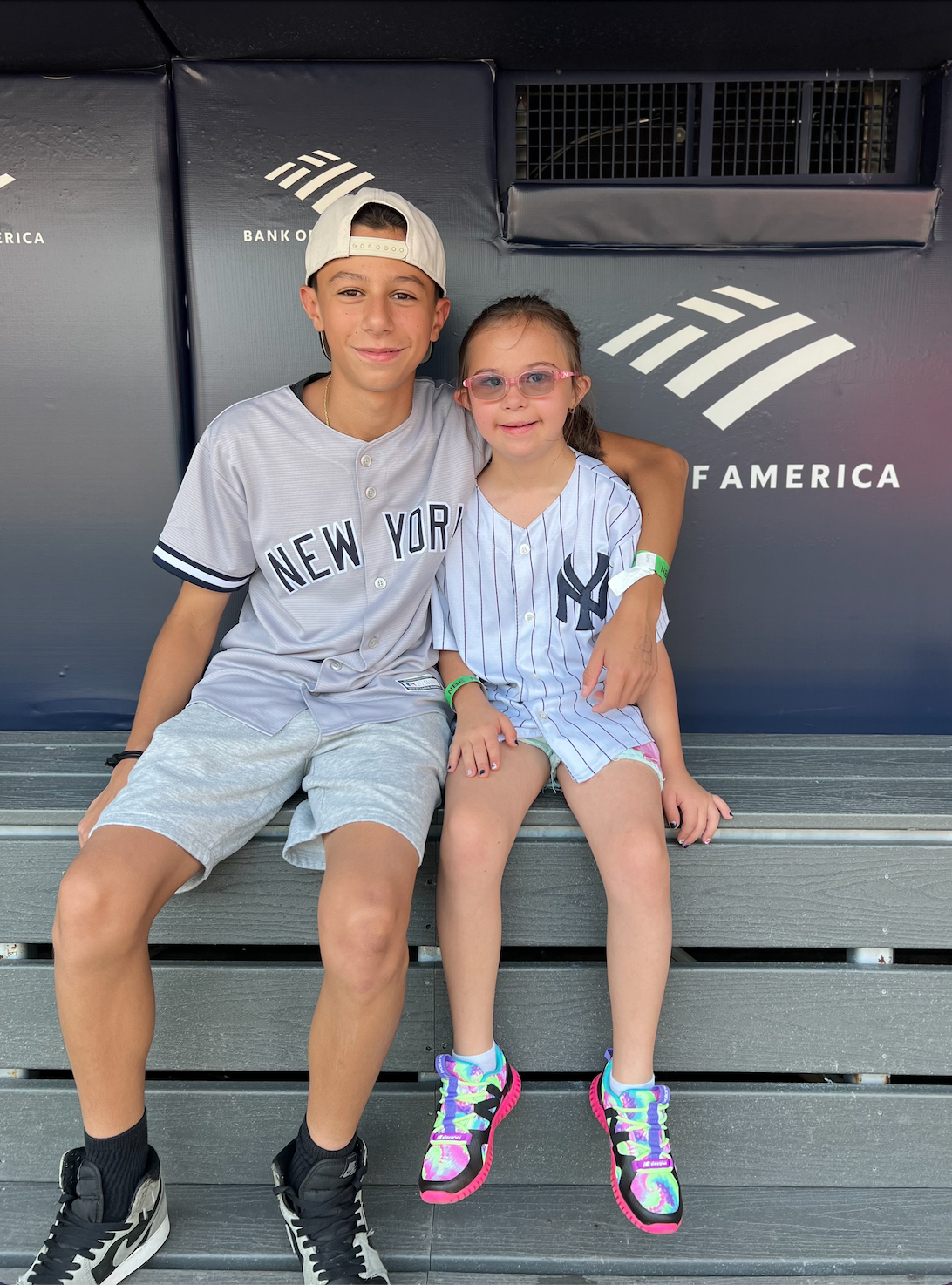 A young boy and girl sitting on a bench with a banking logo behind them, smiling and hugging each other.