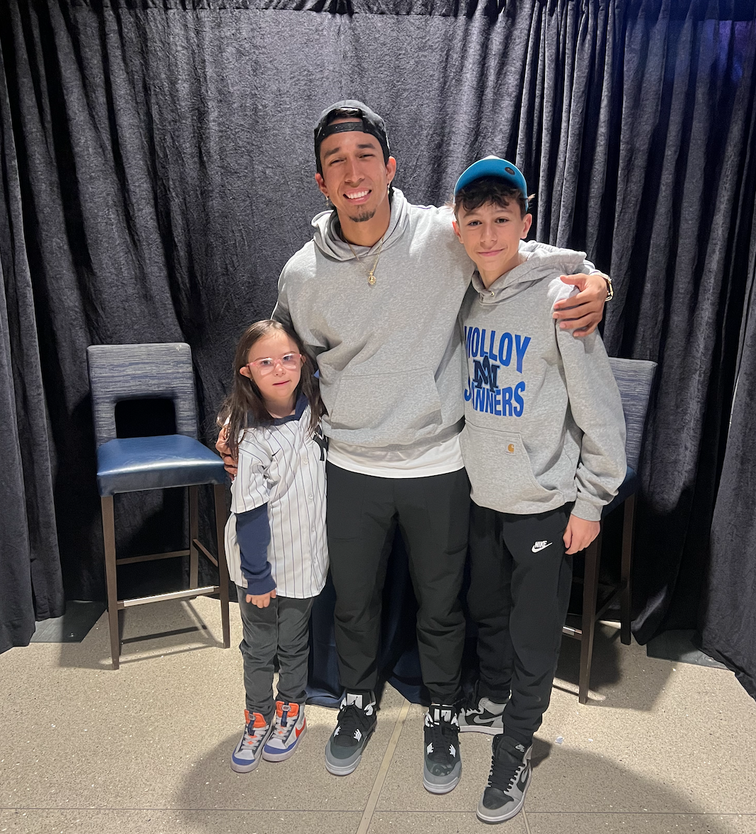 A man with two boys and a girl pose together in front of black curtains, with two chairs behind them.