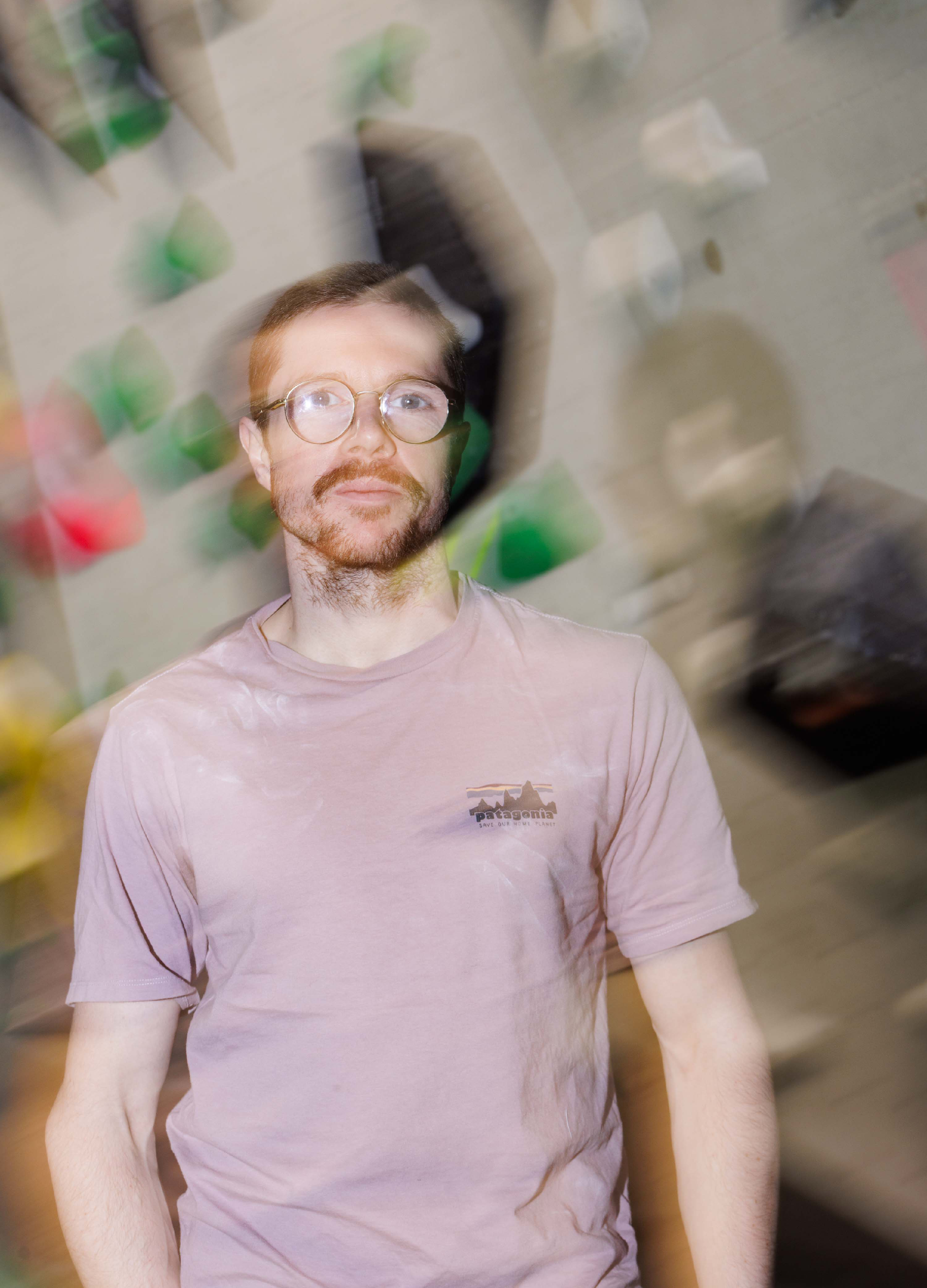 Ein Mann mit Brille und Bart steht vor einer Wand mit bunten Kacheln. Die Aufnahme ist verschwommen und wirkt dynamisch.