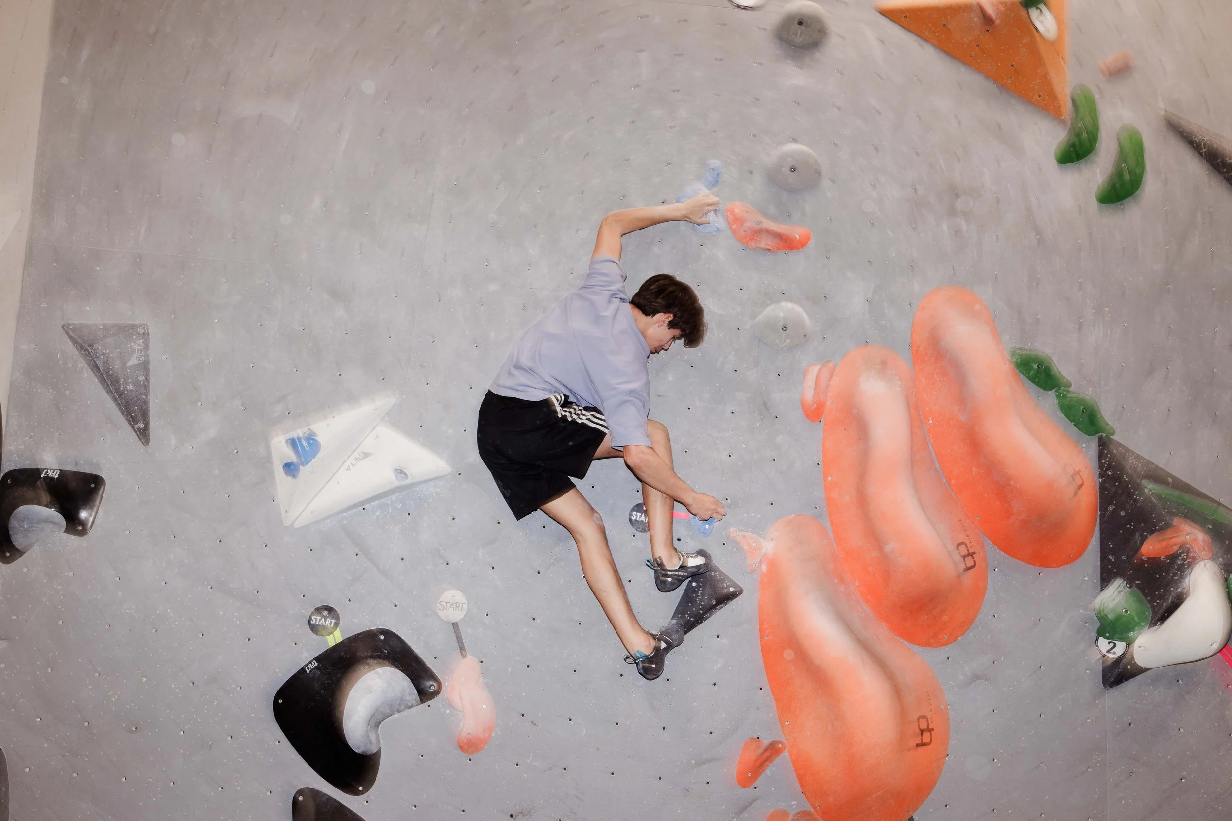 Mann beim Klettern an einer Indoor-Kletterwand mit bunten Griffe und Volumen.