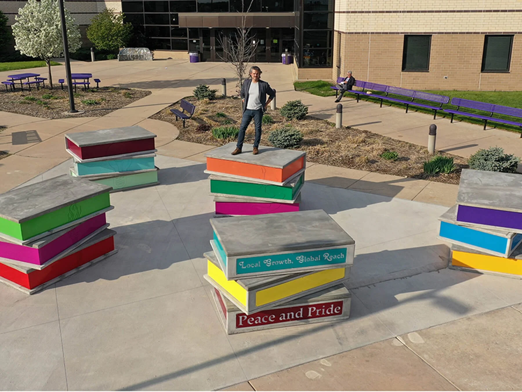 Colorful public art stacked books with motivational phrases printed about Waunakee excellence in education located outdoors at the public high school featuring artist Michael Kalish.