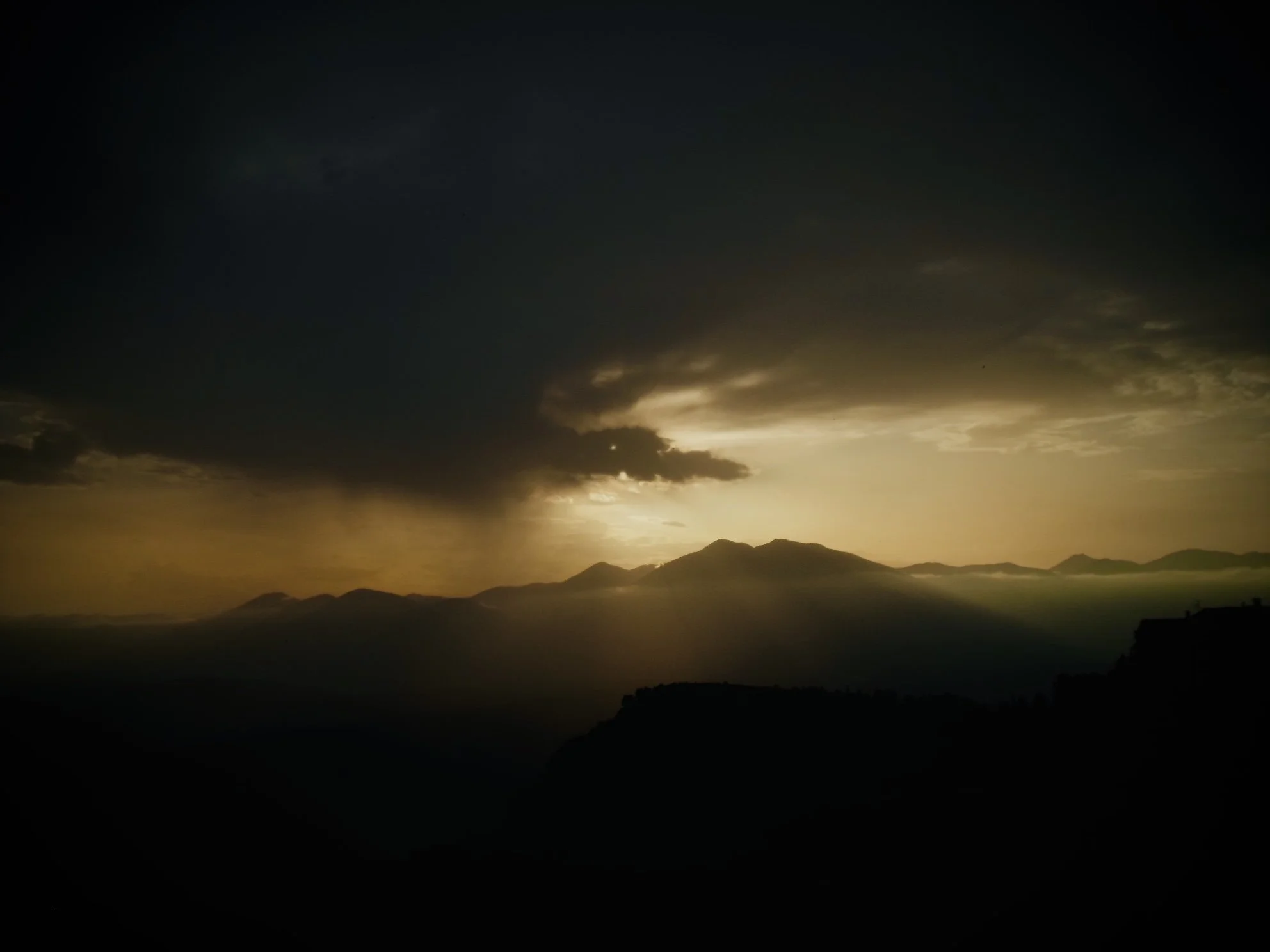 Sunset over mountain range with dark clouds and a glowing sky.