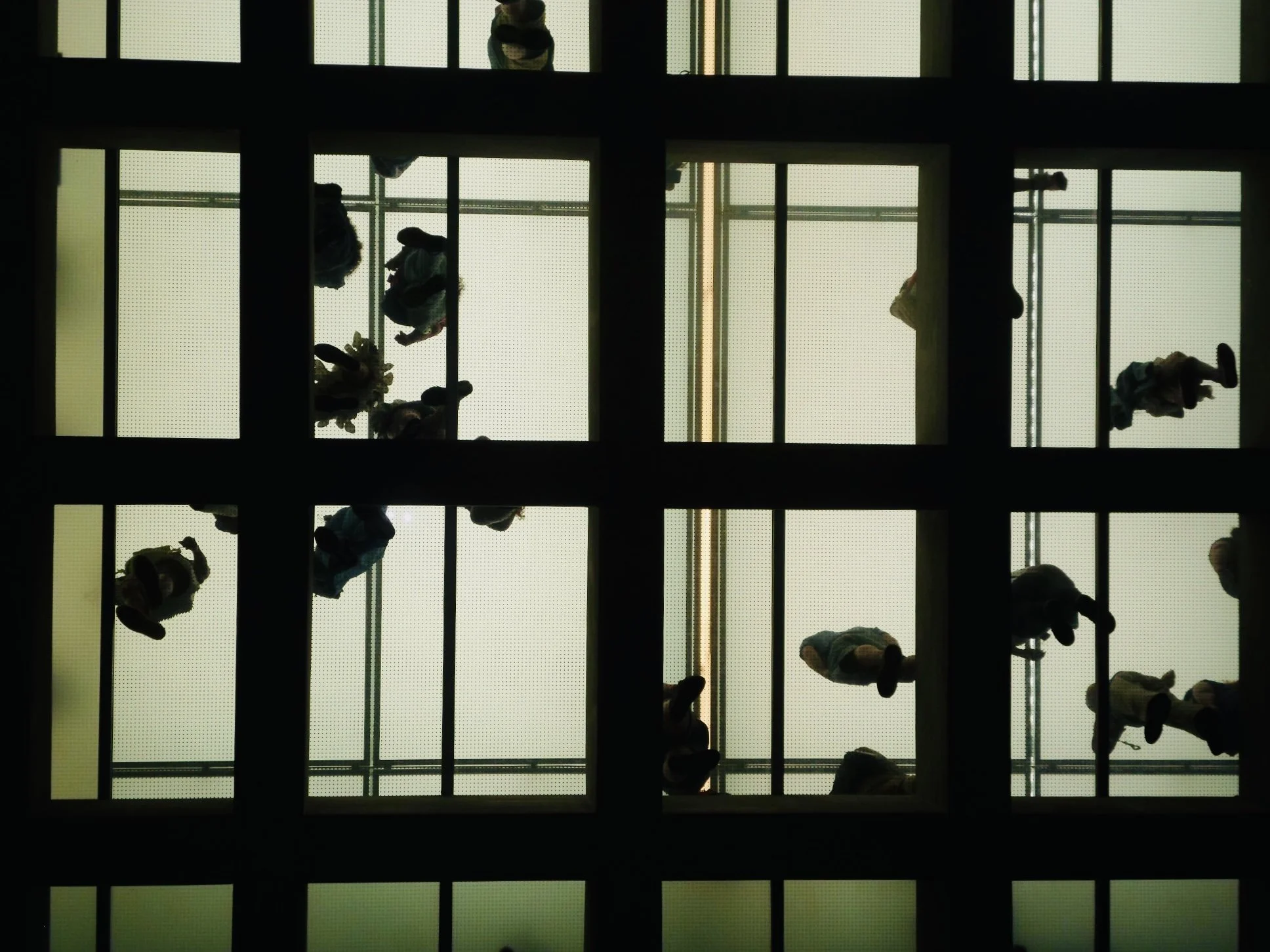 View of people walking on an escalator viewed from below through a grid-like ceiling structure.