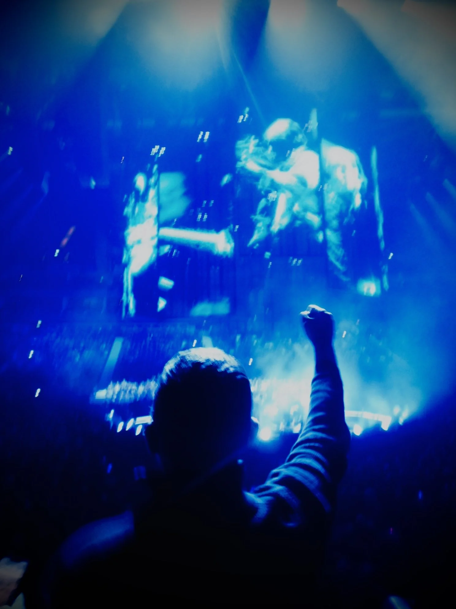 Person with raised fist watching a large screen displaying a futuristic scene or video game, surrounded by vibrant blue lighting.