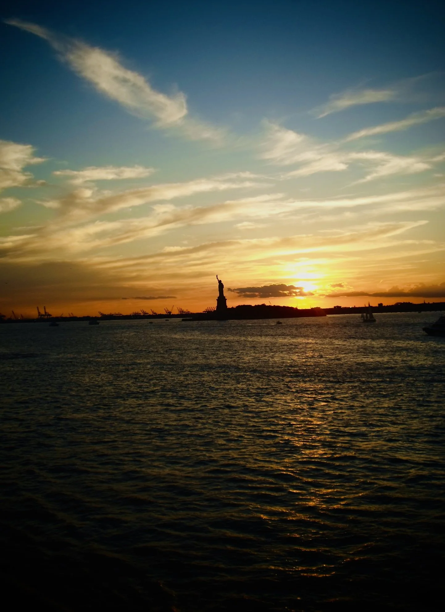 Sunset over water with the Statue of Liberty in the background.