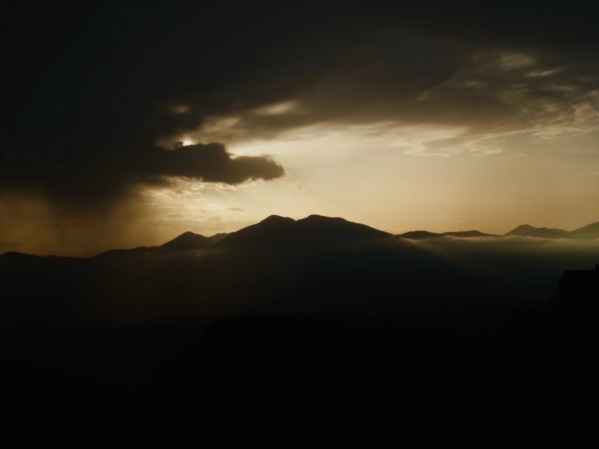 Sunset over a mountain range with dark clouds and a glow on the horizon.